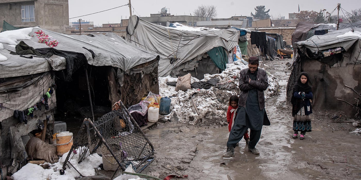 Charqala-e Waziraabad IDP camp in Kabul, Afghanistan. A man and two young girls are standing in the middle of a muddy and snow covered camp.