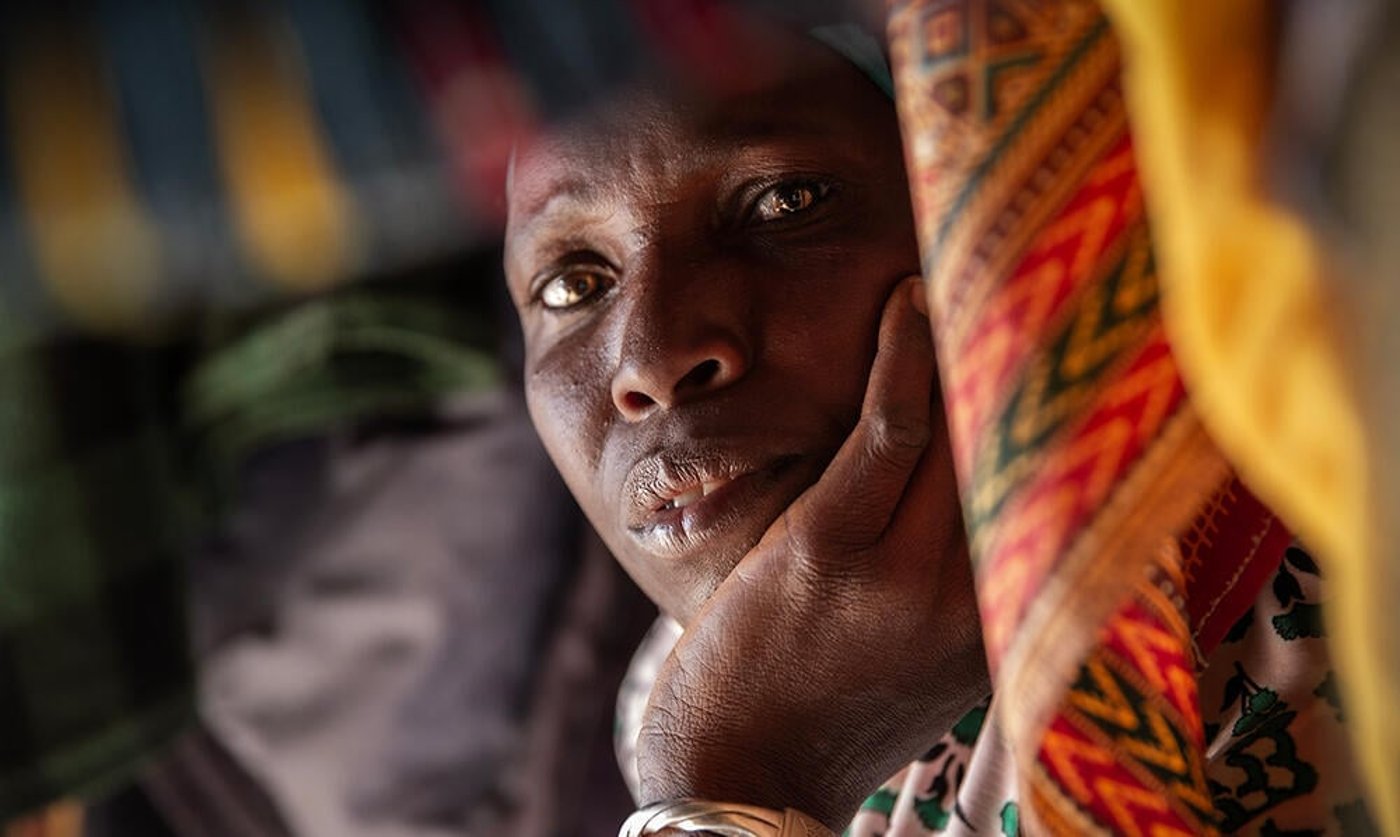 Portrait of a woman resting her head in her hand, surrounded by colourful fabric.