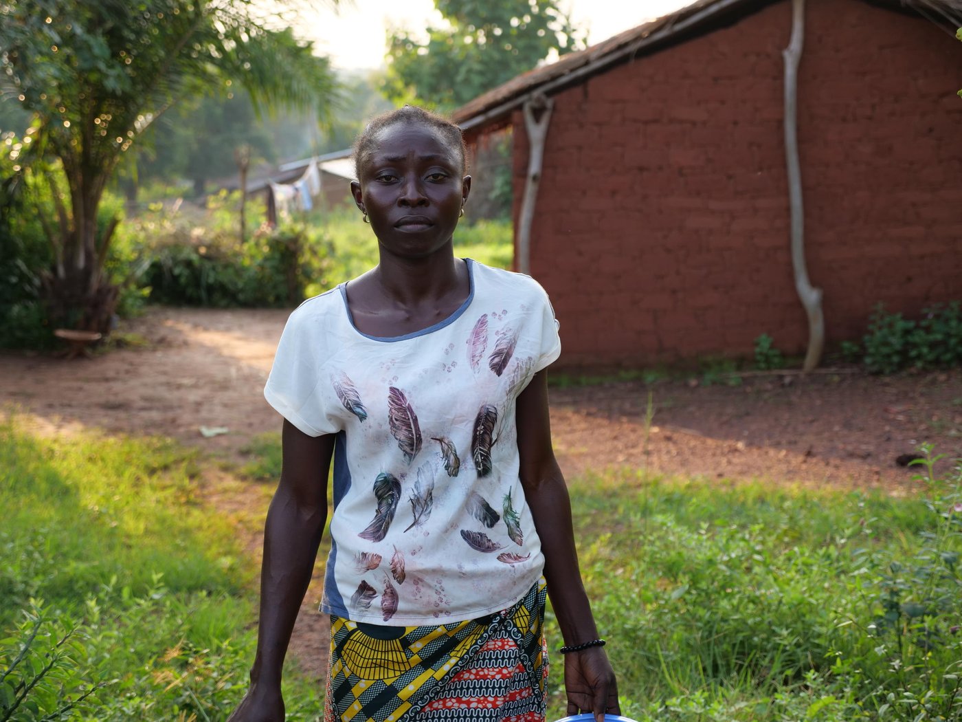 Nuela stands outside of her home in Boali, Central African Republic.

Nuela Ngaiboma is a 29 year old woman originally from Birlo village in Central African Republic. During CAR’s post electoral violence in December 2020, armed groups attacked Nuela’s village, Birlo. She fled and after an arduous journey she made it to Boali to stay with her aunt. In Boali, she received cash assistance from NRC to get back on her feet. She lives with her three childre, (two sons and a daughter) and sells food outside her house in Boali.

“When I was in the fields, I saw many people had started to run. When I asked why they were running, they said an armed group had entered the village and they had taken control of the village. I asked those running if they had seen my children. They said they had just fled as quick as they could. I had no choice but to go back and try to find my children. They tried to stop me from going to the village saying it was too dangerous. I told them I can’t abandon my children, and that I’m going to look for them so we can all stay together in the bush. When I returned to the village, I saw the armed men had taken the village. I heard gunshots coming from all directions. There were no villagers anywhere, there were not even any animals. I found my children and I ran with them to the bush until I reached the edge of a stream. When my aunt here in Boali learned about the attack, She called me and told me to come to Boali with a taxi-moto. I told her that there were no taxi-motos anywhere. How am I going to make it all the way to Boali? So my aunt asked some young people from Boali, to come to try to find me. They crossed through the bush on foot and they found me. It was around 9am when they found me and so we crossed through the bush together. It was around 4pm when we arrived here in Boali. As soon as my aunt saw me, she started to cry. She asked me to stay here and that’s why I’m here to this day. While I was here, NRC came here. They provided me with around $90 in cash in assistance. This helped to reduce my hardship here a little. One of my challenges right now is that my children are not going to school. They’re staying at home because their school is too dangerous. The children can’t go there because the school is surrounded by mines. I have many problems and I’m living in fear. I want there to be peace so my children can continue to go to school. I have so many worries on my mind. Because I am afraid. I am worried that what I just experienced might happen all over again. I just want peace for my country. So that we can work in our fields, go about our business, and see our children go to school while we live in peace. Then we will move past the memories of conflict and live in peace.” Nuela Ngaiboma, 29.

Photo: Itunu Kuku/NRC
Date: 13 July 2021