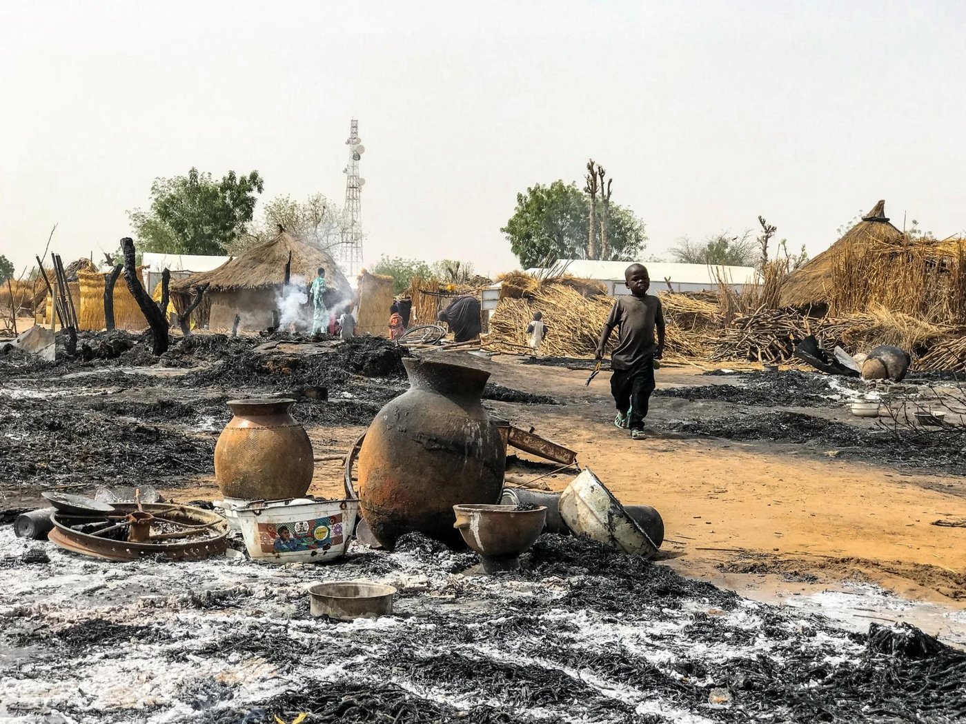 Large swathes of ashes and pockets of smoke can still be seen a few hours after a fire broke at a site for displaced persons in the town of Tungunshe, northeast Nigeria. A child walks by the scene. Credit: Hajer Naili/NRC