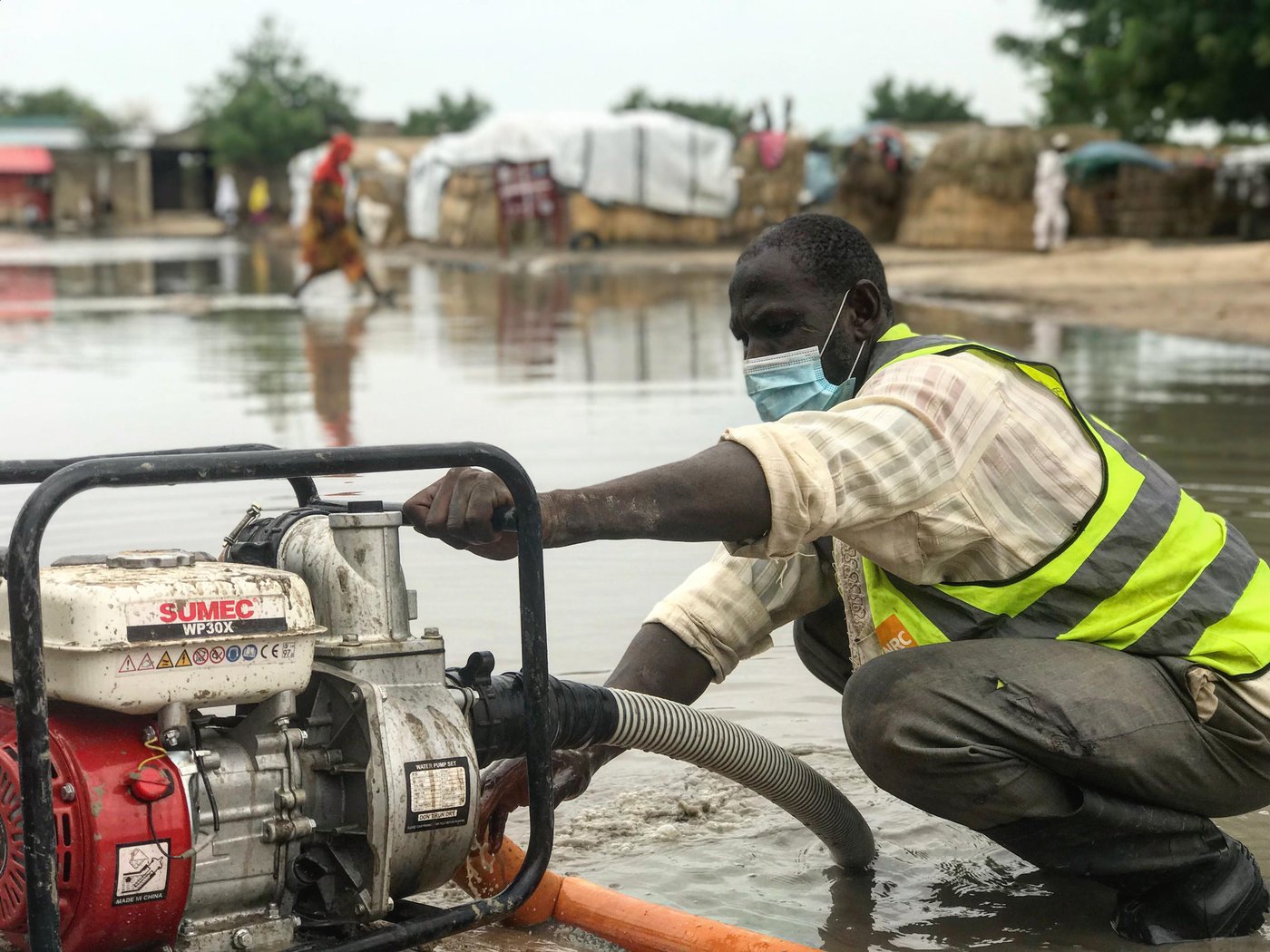 The rainstorms early July have heavily shaken Al Miskin transit camp. In this informal site in Maiduguri, most of the shelters are makeshift and can hardly sustain the heavy rains and winds. Paths and streets within the camps have turned into large mud pools, limiting movements for those disability or the elderly. Stagnant and brown water accumulating next to latrines or water points can quickly be contaminated and carry deadly diseases like cholera.
In this picture, a communty based worker is using a water pump to evacuate the water. This is supported by OFDA.
Credit: Mathilde Vu/NRC