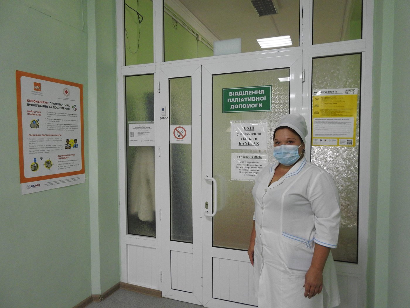 Natalia Sapronova (39) is the head nurse of the palliative care department of the Kreminna multi-field hospital. She takes care of bedridden patients after a stroke who require constant attention. Natalia and colleagues feed the patients, bathe them and fulfil the prescriptions.
“Now we have 33 people in the department. These are mostly older people. However, one person is under 30 years old with a spinal injury and one – aged 30 to 40 – after craniotomy associated with trauma. People usually come from other departments, so they are fully examined,” explains Natalia.
Natalia is showing the entrance to the palliative care department.
Photo: Violetta Shemet/Norwegian Refugee Council