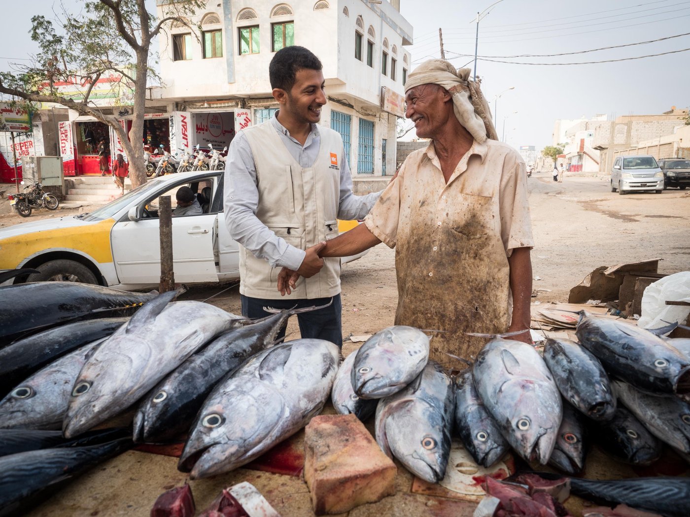 Abdohamid (57 years old – not an IDP).
He worked with fishing authority (governmental sector) and retired.
He has seven children and all the retired salaries of the government sector are little without incentives; therefore, he looked for another source of income covering a shortage.
He has now started working with a mobile trader as an assistant, where they buy the fish whole sale from the fish market and then sell to customers.
This fish markets Al Hotta Lahj (South Yemen) was established back in 1979 by the Yemeni Government, to provide a market place to boost the fishing sector. Unfortunately, for many years the market remained closed or dysfunctional due to successive conflicts and wars in the area. During the 2015 conflict the building was damaged resulting in its complete closure.
Abdohamid and NRC Food security and Livelihood officer Amr Al-Saqqaf is greeting.
Photo: Ingrid Prestetun/NRC