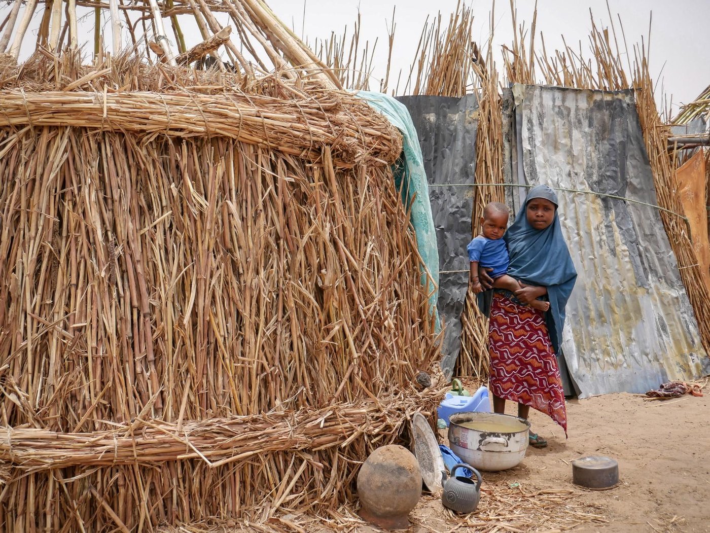 Aisha* holding her young brother while standing near a half-built hut that serves as a shelter to her family. Like over 1.9M Nigerians, this little girl has been displaced by an armed insurgency that began in 2009. Credit: Hajer Naili/NRC
*Name has been changed