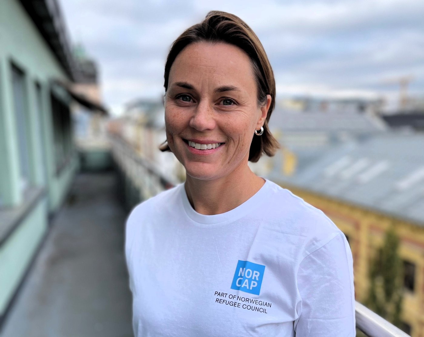 Nordic woman standing on a balcony, smiling. City landscape in the background.