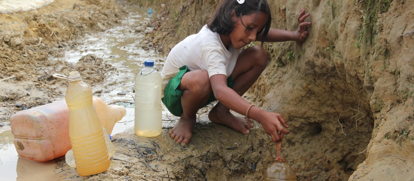 A young girl fetches drinking water from a hole in the ground. Some of the Rohingya refugees prefer to drink water from these open sources instead of using the shallow wells, which they say are already contaminated. (Photo: Ingrid Prestetun/NRC)