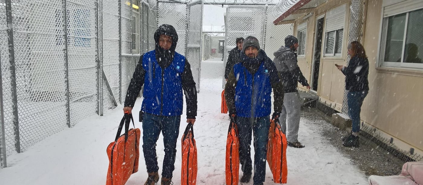When it started snowing in Moria, NORCAP experts lead the set up of new indoor accommodation for vulnerable women and children in the Moria camp in Lesvos. Deployees Kevin Socquet-Clerc (right) and Alan Sulevani are carrying bed stretchers to the facility. (Photo: Anthony Geddes/NORCAP)