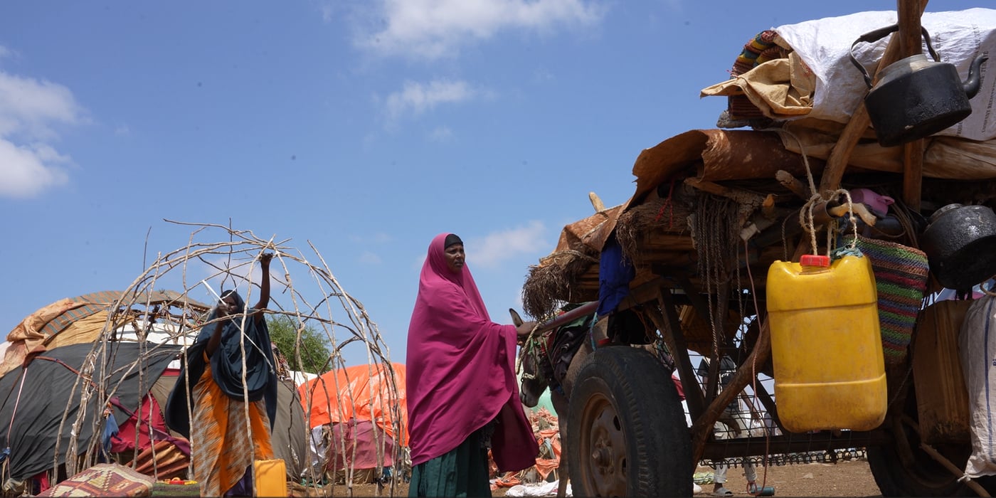 En kvinna i ett flyktingläger står bredvid en åsnekärra.