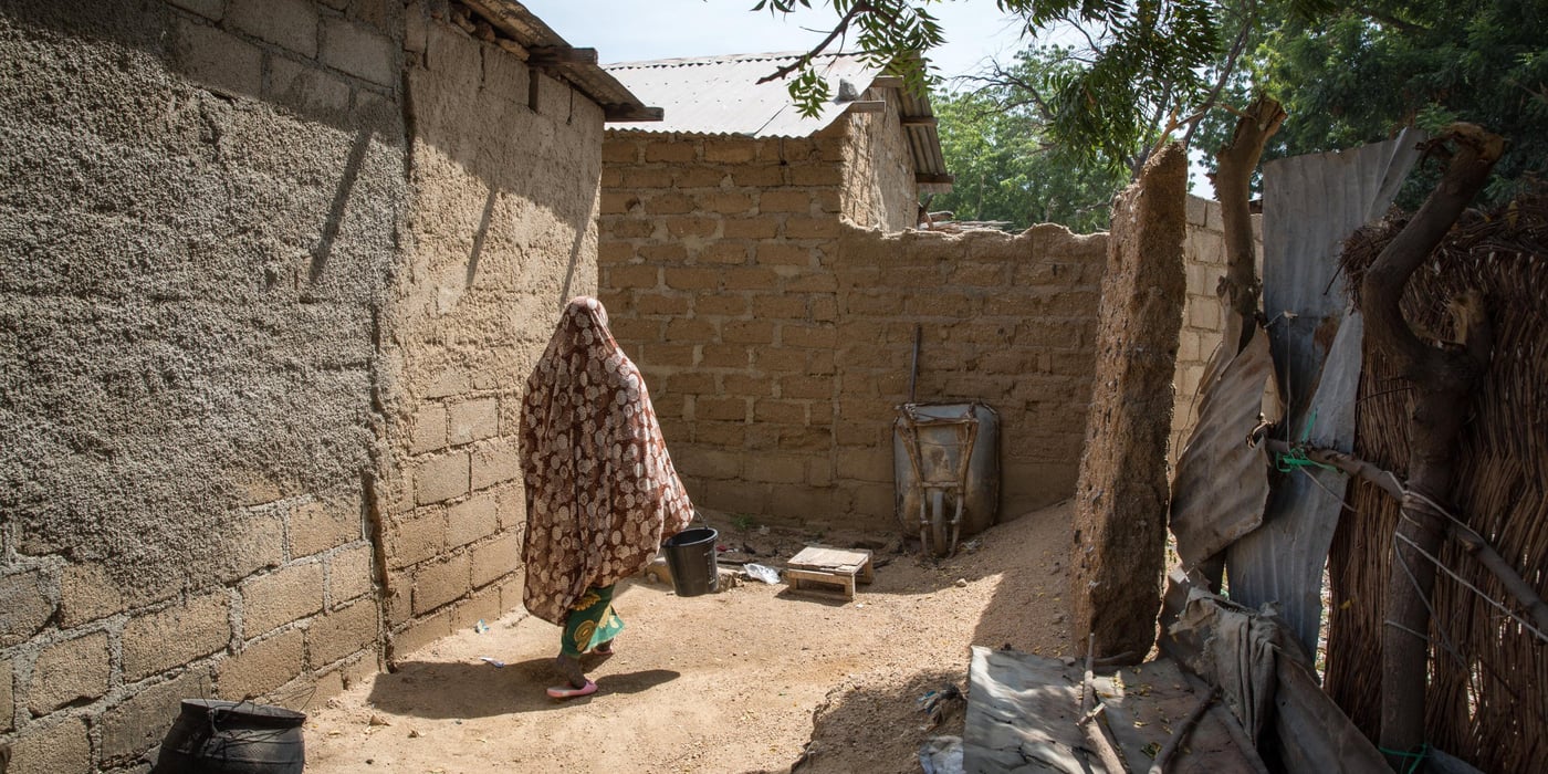 Woman walking in a compound in a rural village in Cameroon. Back turned to the camera. (Photo: Ingebjørg Kaarstad/NRC)