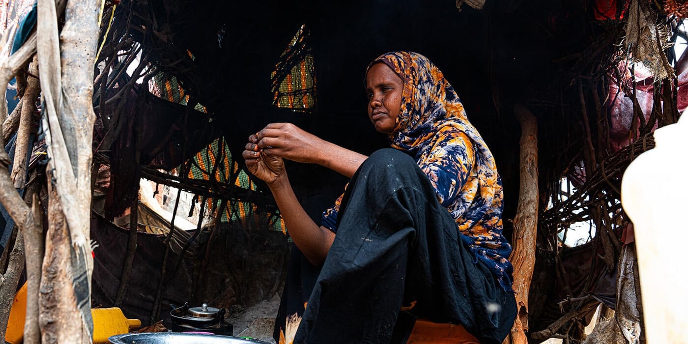 How the Middle east crisis is deepening hunger in Somalia. A woman is sitting on a jerrycan in her shelter, preparing food.