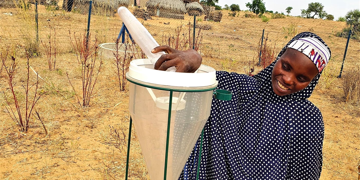 Woman in rural village in Niger checking a rain gauge set up in a field. 