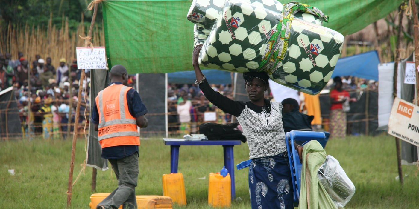 A beneficiary carries what she bought in NRC market organized for displaced & host families in Mahagi territory.
In the picture, the woman carries a new mattress on her head and visibly a sac containing others essentials household items; she has bought in the site of assistance.
In late April and early May 2018, NRC has provided nonfood assistance to over 14,000 displaced and host families in Bunia, Mahagi and Djugu territories, Ituri province in the east of DRC.
NRC has delivered this aid through markets fair where beneficiaries have freely purchased essential household items like pots, pans, mattress, blankets, clothes, etc. Results made possible with UNICEF support via the RRMP8.
RRMP, a humanitarian approach based on a cooperation between humanitarian organisations, managed by UNICEF, was created in 2004 to ensure rapid responses to the humanitarian needs of displaced populations in DR Congo. The programme targets people who have been displaced for three months or less without any assistance.
Photo: NRC/Ephrem Chiruza. April 2018