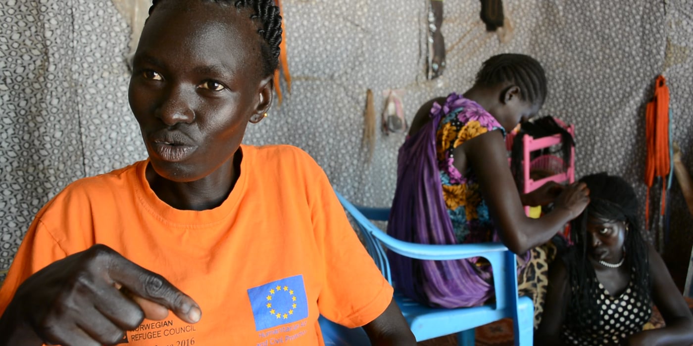 Dorcas is a mother of four children. She fled conflict in Jonglei, South Sudan, although her husband stayed behind. She runs a beauty shop in Nyumanzi refugee settlement, Uganda. “Before the business project, we used to sit idle in the settlement. Luckily, through this initiative, we have participated in training courses in small and medium enterprise management. We have teamed up into a group of four and opened this beauty shop. We also received a start-up kit composed of chairs and hair products to set us off,” she says.
She has rented a 5m by 5m room along one of the busy streets of Nyumanzi refugee camp. She pays a rent of 50,000 Uganda Shillings (11.5 Euros). From the earnings that she gets from plaiting clients ‘hair and selling beauty products, she is able to pay her rent and earn a small income. Although business is still slow at the moment, she is hopeful that it will pick up and succeed in the future.
Photo: Nashon Tado/NRC