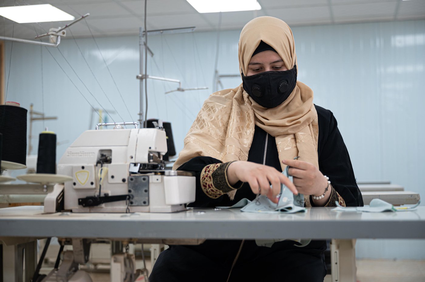 DO NOT USE (embargoed by head office)
Photo: Daniel Wheeler/NRC
Description: Ala (22) sewing some baby clothes as part of a UNICEF contract that the centre managed to secure.
Factual information
First name: Ala
Age: 22
Current location: Za’atari Refugee Camp, Jordan
From: Daraa, Syria. Fled to Jordan in 2012
Occupation: Seamstress at NRC’s youth programme.
NRC beneficiary: Yes, Ala received seamstress training as part of NRC’s youth training programme and now works as a seamstress as part of the programme.
Interview
Ala’s words
“I fled Syria in 2012 because of the heavy fighting. I left on foot at 10pm and arrived at the Jordanian border at 6am the next morning. We travelled at night because we were terrified of being attached on the way. There was around 100 of us and many people were injured.
When we arrived at the border and were met by the army (Jordanian Army) I felt like a drowning person that had been saved. I felt on edge the entire journey and now I had soldiers telling me ‘You are safe now’, it was all so overwhelming.
I live with my five sisters and five brothers. I am the eldest, so I feel responsible for them, and I looked after them during coronavirus.
I found out about NRC’s youth programme after doing a four-month sewing scholarship with a different organisation. I became very passionate about sewing so I wanted to continue my training and the programme at NRC seemed perfect. When I started on the programme, I realised that I still had so much to learn, and it was very intensive but rewarding.
The programme is delivered in three phases, with the first stages being training and the third phase being an employment opportunity.
I live on the other side of the camp and walk an hour each day to get to the centre. It’s a long walk in the desert heat but it’s so worth it.
An average day for me is waking up at 6am and after getting ready, I walk to the centre and we started work at 8:30am. At 12:30am we have a lunch break and then we work until 3pm. After I walk back home, I usually have a nap because the work is tiring but very rewarding.
When asked what the programme means to her, she replies with: “This opportunity that NRC has given me has provided me with financial independence and an opportunity for success in my life. My father is so proud of me and that is very important to me.”
When asked what she wants to do in the future, she says: “In the future, I want to open my own sewing centre for women which has integrity and quality – just like NRC.”