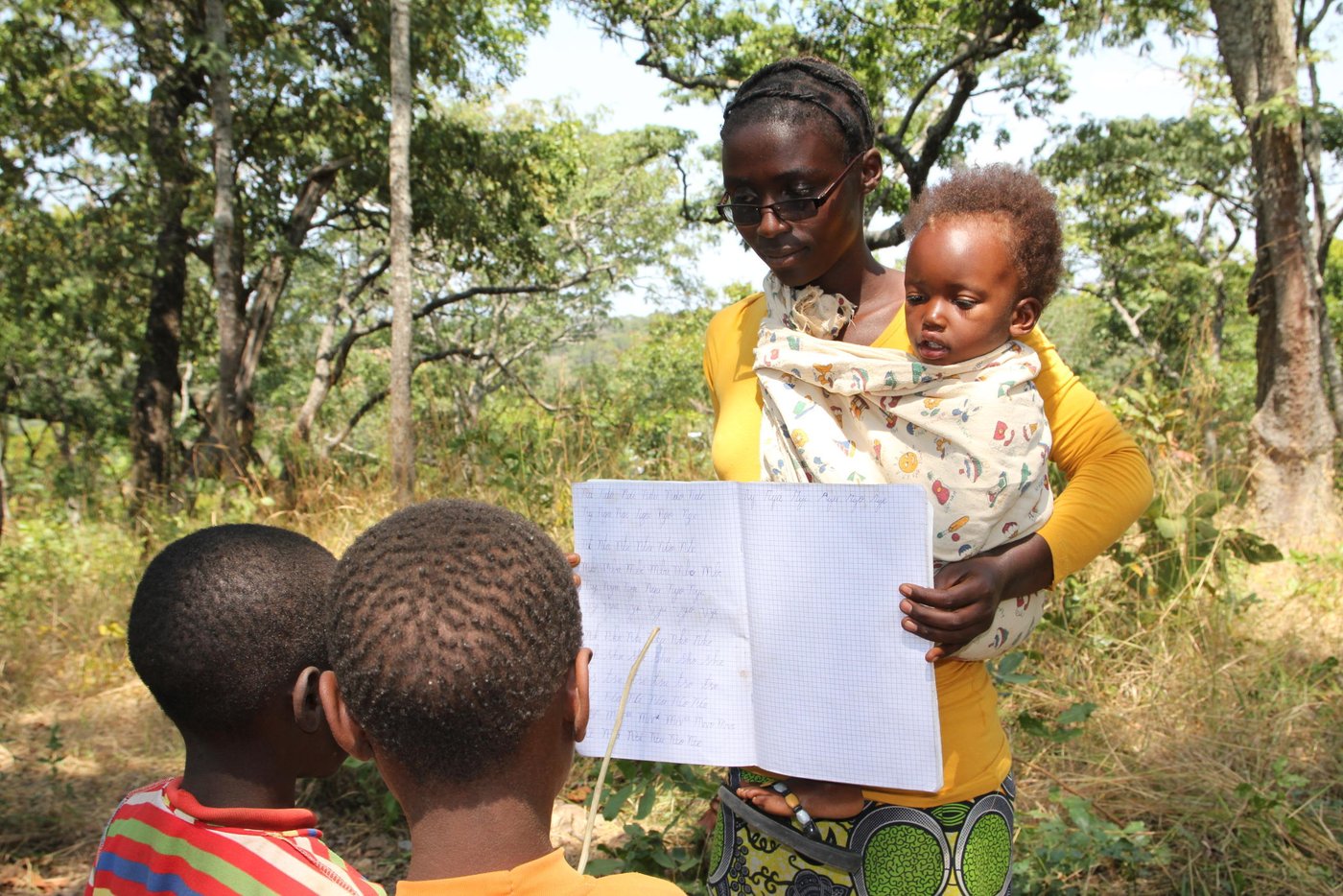 Violette arrived in Tanzania in January 2017. She started teaching in May 2017. Now she teaches Class Two. Her class has a total of 50 pupils. However, the attendance on 14th June was only 13. Reason for the poor show? Lack of books and pens, together with the reason that the pupils were escorting their parents to the food distribution.
A slim and tall young lady, Violette has one child, Bijou Iratabara. The girl’s name means ‘God comes to help people in need’. She had longed for a child for many years and she feels that the Almighty God had finally come to her rescue. Bijou is now two years old. Bijou means gift in French. She is the gift that God has granted to Violette.
Violette originates from Gahandu Commune of Makamba Province in Burundi. Her story from Burundi is filled with traumatizing episodes. Her husband was abducted one evening by members of a dangerous militia group. He had received death threats from some people a few weeks earlier, because of his political affiliation. She fears that the militiamen might have killed him and dumped his body in a river or forest. During those times, it was common to come across corpses of dead people dumped along the streets or washed down the river.
What motivates her to do her job despite hardship? “I am happy when children learn to read and write. It is very fulfilling to see children make progress in their schooling. Now they are trying to catch up, I know that they will succeed, despite the lack of adequate learning materials”, she says.
She always brings her daughter to school. Most times, she is forced to teach while carrying her. This is because she does not have any helper at home. Fortunately, Bijou is always calm and unless she is hungry, she prefers to mind her own business most of the time. There is another female teacher who comes to help in case she needs attention. Violette says that she wants to remain in Tanzania together with Bijou, unless refugees are forced to leave by the authorities.
Quote from violette (June 2017)
“I decided to teach children so that they get knowledge like I got.”
“I teach other children so that life does not stop even though we are in camps, it should continue, they should know how to read and write.”
“I fled before starting to teach. I had just finished my studies. Then the war started before I started teaching children, but I had finished.”
“I fled because my husband, the father of my child, had been taken away because he was not belonging to ruling party. I grew up as an orphan. Whenever I went to my friends, they continued to come looking for my child wanting to kill her. I decided to come here requesting to become a refugee so that my child could live.”
“I like to give knowledge to other children because education is what a child should be given in life.”
“Education is the pillar of development to a child.”
“I like to give children education so that they know how to read and write. Even though they are refugees when they go back to our home they will know how to read and write. They will develop the country.”
“It is difficult to teach. Children do not have books, pens, they don’t have classrooms, schools. A teacher does not have means of transport, bags to carry exercise books on which she writes. But we continue to sacrifice although it is difficult.”
“I live alone. I don’t have anyone to help me taking care of my child. But I continue to volunteer, helping children of my friends, children of my country. We are not paid, we don’t get a salary. Although it is difficult, I continue giving them education so that they also get knowledge.”
“I wish my child, wherever she will be, if she gets education she becomes a journalist.”
“I like to give children education, I like to volunteer. Giving knowledge, giving to other children and my child. When they go back to Burundi they have knowledge and they develop our country.”
Photo: NRC/Ingrid Prestetun
