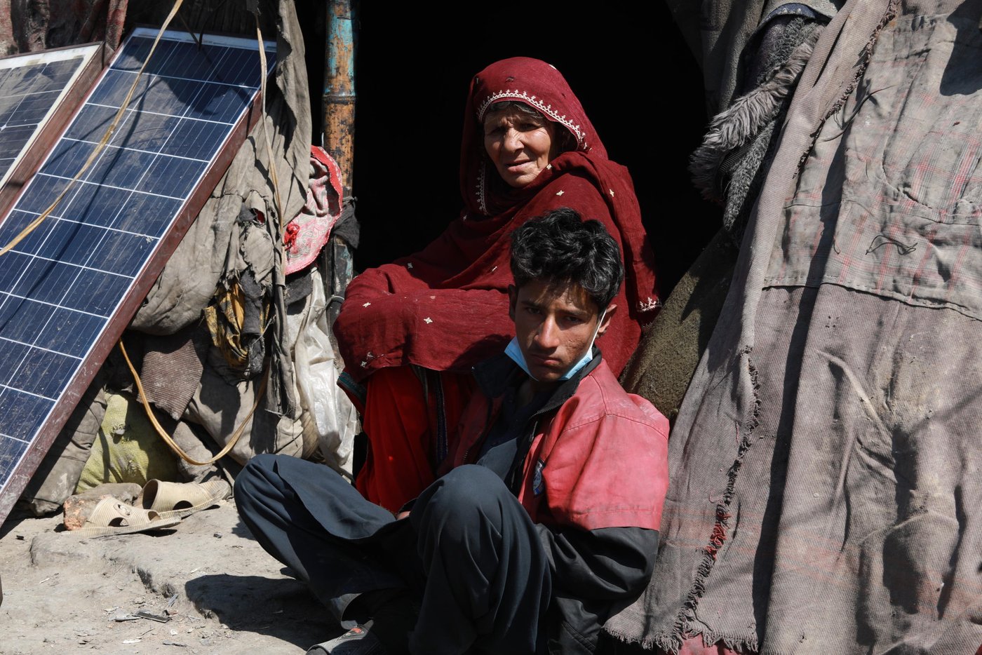 Shayista Gul, 60, and her son Esmatullah, 17, sitting in front of their makeshift shelter on the outskirts of Kabul city. The family have been living in this IDP settlement for 13 years now since the time they have been returned from Pakistan where they lived as a refugee. The family has no source of income since Esmat lost his father in an explosion in east Nangarhar province who was the primary income generator of the family. Now, 15 people, including Shayista’s daughter and her children, who also lost her husband in the same explosion are living in a two-room makeshift home.
Quotes from Shayista: “Since the outbreak of this diseases the price of food items are raised to double folded. I went to a nearby shop this morning to buy soap and detergents, but I could not buy it as the price was increased. Now, I’m washing my clothes only with water without using any detergents.” “we are staying on government owned land and there is no borewell or water tap close to the settlement. It takes at least five minutes to fetch water from a well inside another colony.”
“We usually rely on community donation here and I heard that price of a bag of flour had increased by 1200 (approx. $16) yesterday and in this case, families might not have sufficient food themselves to help us anymore. We noticed that everyone who could afford was rationing foods and we are just left like that. If things get worse in the coming days or weeks and food and vegetables falls short and shops remain close, we will be left hungry and might lose our loved ones.” “even if the government ask us to stay at our homes, we can’t. we have to collect scrap to feed our children. If not, we die out of hunger and not having food. If Coronavirus do not kill us, hunger will, definitely.”
Photo: Enayatullah Azad / NRC