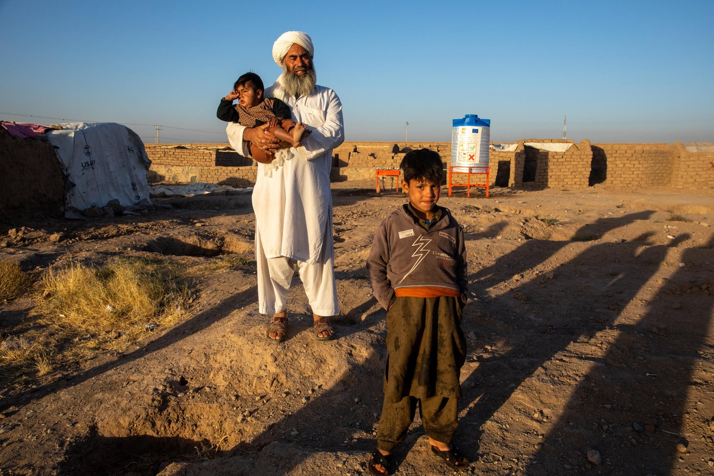 Mullah Mohammad Ayub, 42, is one of the countless displaced persons in Hirat whose heart is beating for his hometown, but can’t go there. He and his family of five are forced from his home in Bala Morghab district of Badghis province three years ago. Since then, they live in an IDP site for drought and conflict-affected families in Shaidayee camp. Some 7,000 households live in a private owned land in Shaidayee. Less than a kilometer to the east is another IDP camp that hosts an estimated 40,000 households named Shahrake-sabz. These families have been displaced from Badghis, Faryab and Ghor Province three years ago due to drought and conflict.
Ayub desparately looks for the betterment of the security situation in Bala Morghab where he can go and start up with agricultural activities and livelihoods.
“I follow the news of my hometown very closely through the radio. We don’t have electricity connections or a television here and I usually listen to the radio on my mobile phone that I charge with a small solar panel. There wasn’t any concerning news on my district and I went to see if I can go back to home with my family. I went there and I spent only one night. There was fighting ongoing and I was about to be killed. The security situation is volatile everywhere in the country and the media ignores many news if it is not the matter of collapsing a district center or a province.”
“It is very hard to live here and I have taken a lot of personal loans now. I am cleric and if I ask for a loan people do not say no to me. I have taken loans from my brother-in-law who lives in Turkey, cousins in Iran and people in Badghis. I have a rich and fertile field in Bala Morghab and if there is any chance to go back I can work hard and pay their money within two years or less. But we are stuck here. We can’t go back home and neither do we work here. If there is peace, I won’t stay here for one extra day. I don’t know if peace will prevail sometime soon in this country but I hope for it. This is not the life we do here. I was teaching students and we had everything in life we needed. Here, we do not even have water to wash our hands and face. We are very thankful to NRC for providing water for us. Accessing water was a great challenge for us, especially during the hot summer season. Children and women were providing water for the whole family. It was taking them hours to find a good willing neighbor who was helping us with a small water container. Sometimes we were also paying for water. Now, we have sufficient water at our doorstep. We have enough water for cooking and cleaning. We are not roaming around the camp for a water container and even the neighbors are happier that we are not disturbing them anymore.”
Mullah Nohammad Ayub knows the importance of education and though he struggles to provide food for his family, he is keen to support his children get education. He has convinced the headmaster to admit her daughter and two more girls from the camp and teach them for free as there is no school in the camp for displaced children.
“Those who are running a school knows who we are and what is our financial status. I went to a private school nearby and explained that we can’t afford the fees you require and as their parents we have failed to provide them the education they are entitled to, but it is up to you now to help them along the right path. The headmaster offered scholarships for three girls. Now, my daughter, Bibi Amina, 8, and two of her friends Brishna, 10, which means (brightness) and Khanzada, 9, are attending class. We just provide stationaries and transportation for them. Education is very vital for children and will help them move out of poverty when they are young.”
When I asked him why is he look much older than his actual age and the reply was: “I have lost three sons in this war. Three young sons!”
Photo: Enayatullah Azad / NRC