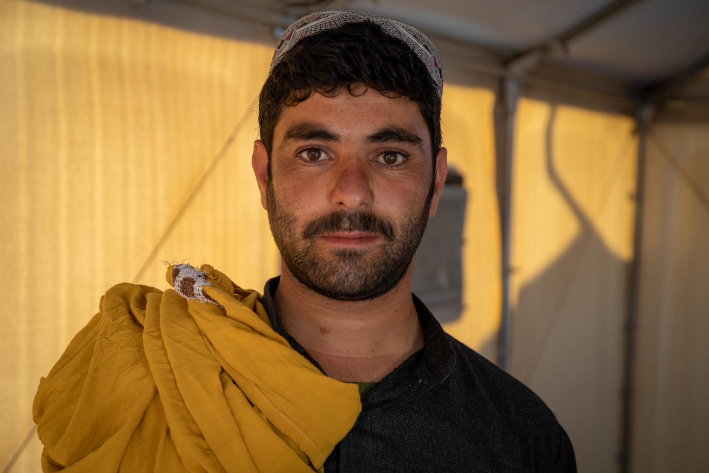 Mohammad Amin, 24, (Anonymous name) and his family are from Qadis district of Badghis. Four years ago, both his father and brother were killed by a non-sate armed group in Qadis. His father was the community head and the Afghan National Army (ANA) often visited him in his home. The non-state armed group executed them for supporting government.
“They were not soldiers nor government employees. Government officials were usually visiting us because my father was the community head. We can’t say no to our guests when they come to visit you at your home. And it is our culture to offer them tea and sit and drink that with them. Like today, I am the community head here and you came to visit me. I can’t refuse meeting you in my home.”
“If receiving a guest at your home is a crime, that was the only crime my father committed. Now, I have to feed three families of fourteen people and thirteen of them are female. My brother and father were on a motorbike on their way to Bazar when they were shot to dead.”
“When they were killed, we fled from the area. I was the only male member of the family and the rest thirteen were all female. I was frightened and needed to protect the family. We fled to the mountains first with all the children and women because there was a rumor that they would come and kill everyone at home. We spent a night in the mountains and came down the day after, got a car and fled from the area.
Now, it has been four years that we live here in Hirat. We have erected our tent on a private land in Kahdistan area, later the government and NGOs asked us to move in Shahrak-e-sabz. We couldn’t make a makeshift house for us there and now, this is the governmental land and we have a roof over our head.”
Amin has to feed fourteen people. There is no work for thousands of displaced people in Hirat and he doesn’t have any other source of income. The. Covid-19 pandemic has deteriorated the situation for him and he has married off his three sisters to feed the rest of the family. There is him, his wife and two little kids. His mother with four daughters and his brother’s widow with her three daughters.
“I sold three of my sisters and they are seven, nine and eleven years old. The only one remained at home is a three years old sister. She was not born when my father was killed. I need to take a bag of wheat flour (50kg) for the family once in a week which costs 1,600 to 1,800 AFN. We have no income here and it has been eighteen months that we have not received any assistance like food or cash. We received soaps and shampoo some six months ago. People are starving here and you gave them soaps, shampoos and toothpastes to do what? Covid-19 did not kill the displaced population and this time it will because they are weaker than six months ago and many will starve to dead this winter.”
“In 2014, when my father and brother was alive, I wanted to go to Europe for better life opportunities and work and wanted to seek asylum in Germany, but I was arrested by Turkish border police and they deported me back to Afghanistan. Wish I had arrived there safely, now my father and brother would have been alive and my family would not have suffered this much.”
Photo: Enayatullah Azad / NRC