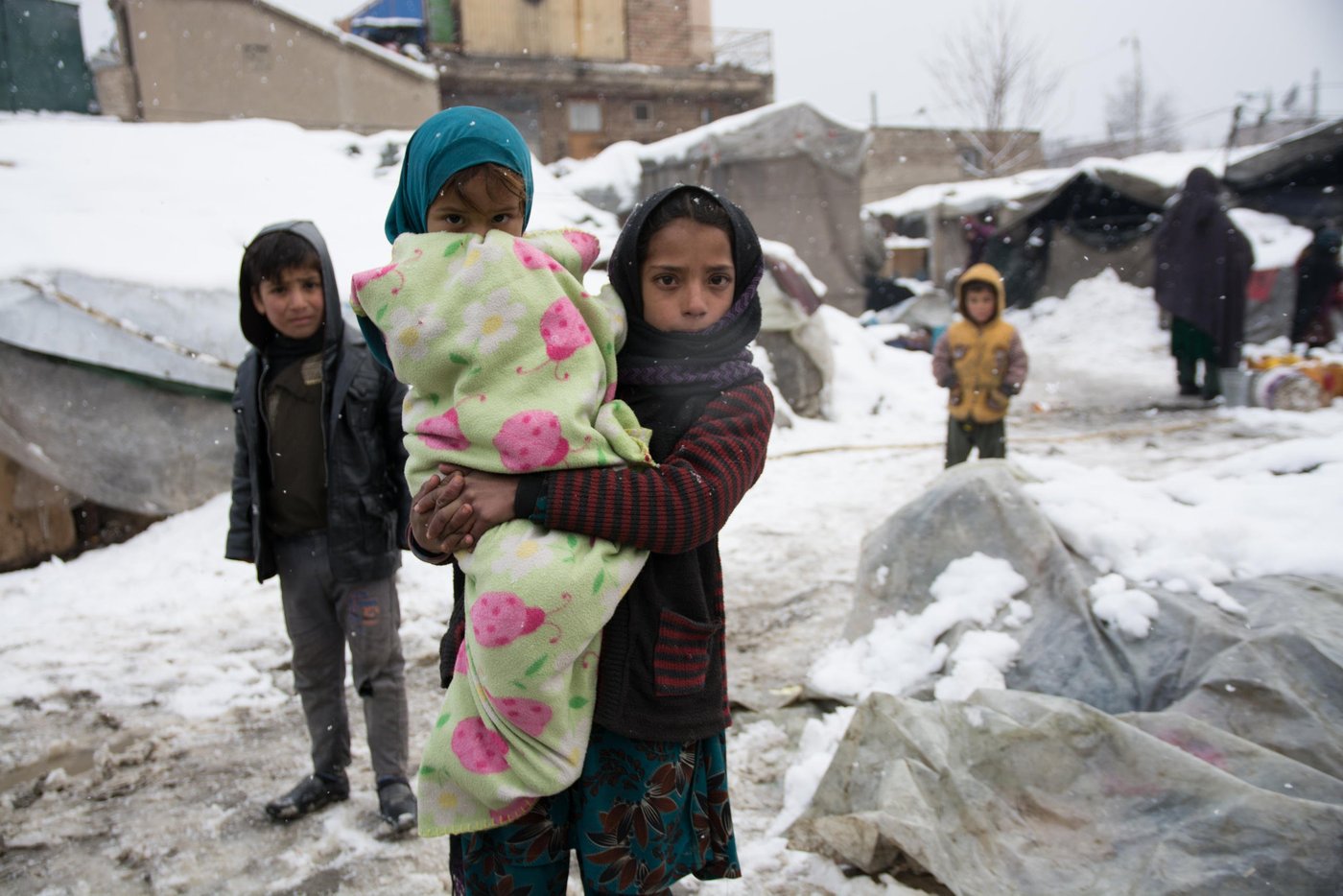 Nazia, 11, taking care of her little sister Palwasha, wrapped in a thick blanket in one of the informal settlements in Kabul. The children are experiencing their third winter in this settlement. photo: NRC/Enayatullah Azad