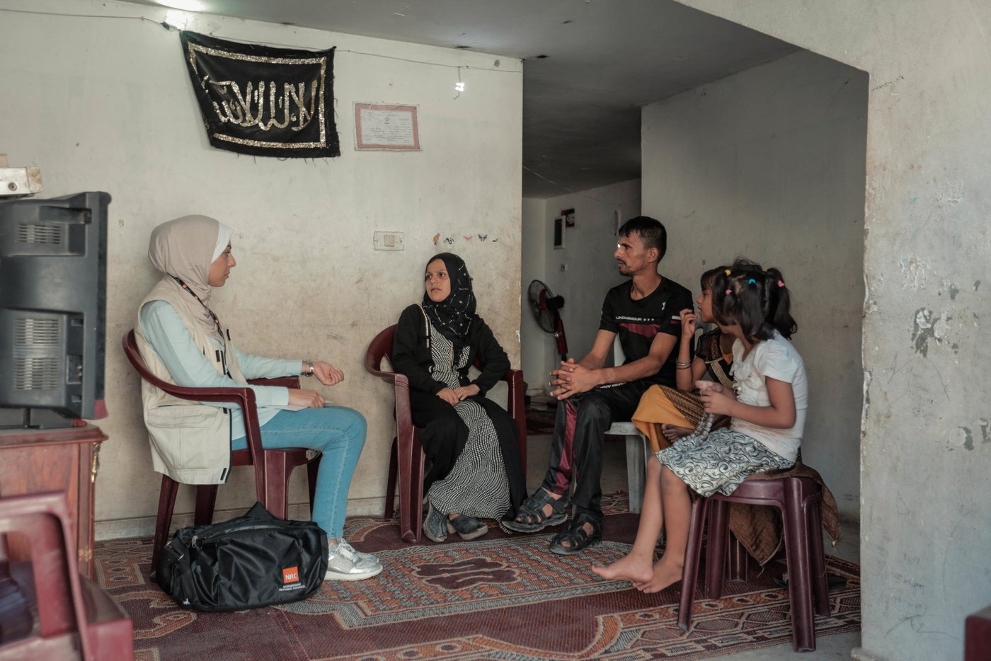 NRC Shelter Technical Assistant Aya Abu Ramadan (left) meets the Al Zaharna family inside their rented apartment. To her immediate right is Eitidal, 30, her husband Medhat, 33, Remas, 7, and Layali, 11.
“Just before NRC’s support, the landlord had warned us that we have a short period to search for another house, as we had four months of unpaid rent,” said Eitidal. “We remain worried about what will happen when the six months of cash for rent assistance ends and fear eviction.”
Eitidal and her family have been renting their home in Jabalia for the past year. Less than half of households surveyed by NRC have lived in the same place for more than one year, due to their inability to pay rent. 
The apartment’s poor condition, limited ventilation, mice, and cockroaches are still better than living on the street. 
Out of the 522 households, 23 per cent live in homes that fail to meet the minimum standards set by the Shelter Cluster, an inter-agency mechanism that coordinates the humanitarian shelter response, while 4 per cent live in informal shelters such as storage units, which lack even running water and sanitation.
The family has been evicted twice before over accumulated rental debts. Their previous landlord cut off their electricity, threw their furniture out on the street, and submitted a complaint to the police. 
Too often, Eitidal says, she finds herself without food for her children. In May, her daughter, Rimas, tired and hungry after school exams, ate leftover food thrown away by a nearby restaurant, and had a nasty bout of food poisoning.
Since hearing of the story, the restaurant owner has given the family cooked rice for free, and whenever Eitidal has nothing to feed her kids, she sends them there to eat. Other times, Eitidal’s husband brings home spoiled vegetables from the market and every once in a while they go over to their relatives for meals.  
Even drinking water can be hard to come by. 
“We do not have either a water tank or a jerry can,” said Eitidal. “I send my daughters to the supermarkets to fill 10 water bottles at a cost of one shekel [US$0.28]. Sometimes we do not have one shekel and must hope on the goodwill of neighbours.”
According to the 2018 food security survey by the Palestinian Central Bureau of Statistics, 68.5 per cent of Gaza’s households are food insecure, with 47 per cent severely affected.    
Eitidal’s family receives cash assistance of 1,000 NIS (US$284) from the Ministry of Social Development every six months and UNRWA food vouchers every three months. Eitidal has had to sell the food items she purchases with these vouchers for half their worth to have money for medicine, gas, and other basic necessities. Otherwise, they rely on the goodwill of relatives and strangers to survive.
Around six months ago, Eitidal, in desperate need of money, promised the same food items she was due to receive to two people. When she was unable to provide the second person with the items, he made a complaint to the police.  
“The police came to take my husband to jail, and my daughters started to cry,” said Eitidal. “Since then, they have become terrified every time they see a police officer.” 
Eitidal’s husband spent 21 days behind bars. 
More recently, Eitidal signed a promissory note (a promise to pay outstanding debts by a fixed date) for debts in the amount of 220 NIS (US$63) to a supermarket owner, who involved the police to force the family to pay the full amount in installments.  
“The day we receive the cash assistance from the Ministry of Social Development is the worst ever,” said Eitidal. “All the lenders come asking for their money.”
Photo taken on 21 August 2019, Jabalia, northern Gaza.
Photo: Ahmed Mashharawi/NRC