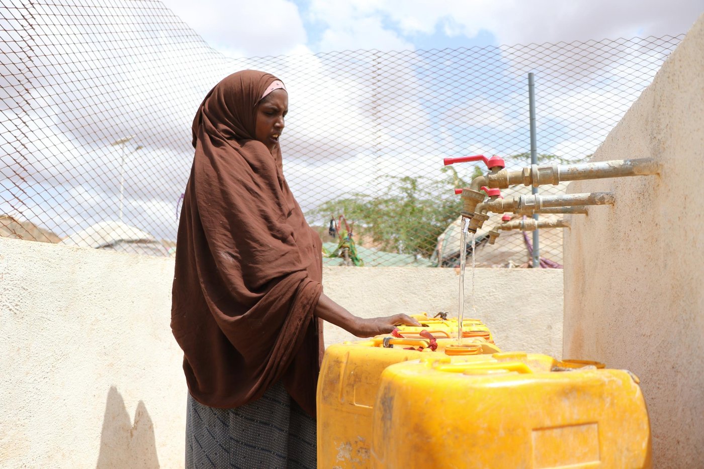 Hudur is a town in the south western Bakool region of Somalia. It serves as the province’s capital and is the center of Hudur town. The main supply routes to and from Hudur town are blocked and are controlled by Al Shabaab. For the last seven years, food and other commodities were transported only by donkey carts but in the last two months, the situation was getting worse.
All roads leading to the main towns of Baidoa, Mogadishu and Beletweyne remain blocked, and no goods are allowed into the Hudur town. The Means of transport available to traders and consumers is airlift resulting in high transportation costs, which further adds the cost of goods to the consumers. The scenario contributed to scarcity and high commodity prices. Rainfall harvesting is a significant source of freshwater to Hudur residents: as such, below average GU rains leading to low crop yields and drying up of (Warcadey and shallow wells), means the situation is fast deteriorating.
According to local authorities and PRMN reports, an estimated population of 4,950 households, comprising 29,700 individuals, are confirmed to have fled their homes mainly from the peripheries of Hudur town. The displaced households were unable to take their belongings and essential household assets. A significant portion of the affected populations were older people, children, pregnant and lactating women, and persons with disabilities, observed mainly arriving on foot or by donkey.
Currently, there are 20 active IDP sites hosting 9,263 households or 55,578 individuals. Compared to the last site verification conducted in April 2021, there was an increase of 3 IDP sites, 4,950 Households or 29,700 individuals. The projected number of people expected to face crisis of (IPC Phase 3 or higher) and would require urgent humanitarian assistance in Hudur for the period July to September 2021 is 21,300.
Hudur town, is under complete siege. The supply routes to and from Hudur town which are blocked and are controlled by Al Shabaab. Food and other commodities are transported by only air which further escalated the price of the commodities to the consumers. Hit and run attacks to the town mainly during night hours, occur and the residents were observing a rehearsal of a big AS attack to the town. For two consecutive years, the livestock and agricultural productivities has been below normal in many parts of Bakool region due to poor rangeland conditions and below-average rainfall, leading to low income from livestock sales and limited household availability of livestock products and local cereal stock.
Most rangeland areas have received below-average rainfall amounts during the last Gu season. The current dry conditions are expected to aggravate the already poor malnutrition status within the Hudur district of Bakool region. There is persistent food insecurity among IDPs and vulnerable host communities in Hudur district with limited operational presence of humanitarian agencies in the area.
A quick solution was needed to respond to this desperate situation, so in 2020, the Norwegian Refugee Council (NRC) implemented the project “Integrated protection response to vulnerable and displaced populations in Hudur district.” This was funded by the Somalia Humanitarian Fund (SHF), and involved in both WASH and protection activities. The WASH facilities has made a huge impact and provided free and safe drinking water to over 13,500 individuals.
Muslimo Abdi Ibrahim, and her family of nine children (3 boys and 6 girls) have been living in Dondardid IDP camp since fleeing from their village in the rural areas outside Hudur. Due to the lack of sufficient water, to save water for only cooking and drinking, Muslimo said that they had to limit the bathing times. They used to take bath only two times a week.
She also said that water was very important for themselves and they needed water more than anything else in their life. Thanks to NRC’s immediate response, Muslimo and the other vulnerable IDP communities in Dondardid camp are no longer to worry about water. They can now access water effortlessly.
“We have free and safe drinking water in our doorstep. I can comfortably fetch enough water. My family can use water for drinking, cooking, washing clothes and bathing. Nothing to worry about at the moment,” she said.
Seven years down the line, since the siege, the communities in Hudur district could not walk the streets at night due to darkness and fear. All business along the main and small streets in the town closed at 5:00 pm in the afternoon. No movement. No social-gathering at all, and the residents locked themselves up in their homes.
“After the sunset, everyone goes home. People could not walk anywhere in the town specially women because of fear. Everything can happen under the cover of darkness, so we remained home,” says Habiba Ali Borow, a local resident in Hudur district.
The Norwegian Refugee Council (NRC) rehabilitated thirty-two solar streetlights in one of the main streets in Hudur district. This was part of NRC’s integrated project funded by the Somalia Humanitarian Fund (SHF). Life for local residents changed since the rehabilitation of the solar streetlights. They are now doing business and socializing on the streets after sunset.
“After years of fear, and being in darkness – the main street has been illuminated. The darkness is over now. When the lights started working. We felt like we get out of a prison, we can walk freely at night to shop or visit friends, relatives and neighbours without any fear,” she said.
Ruqiyo Ibrahim, a mother of seven, and the owner of sells milk along the main street, has seen her small business doubled since the solar streetlights were rehabilitated. Business along the main street including shops, restaurants and small business can now stay open at night as long as there are people who want to shop. It’s a huge blessing to have the solar streetlights and the lighting scheme provided opportunity to all the people.”
“Young people are enjoying tea in outdoor tea-shops because of the solar streetlights. Children are also playing football along the side of the main street, and we thank NRC and SHF for that” said Ruqiyo.
Text: Abdulkadir/NRC
Photo: Abdulkadir/NRC