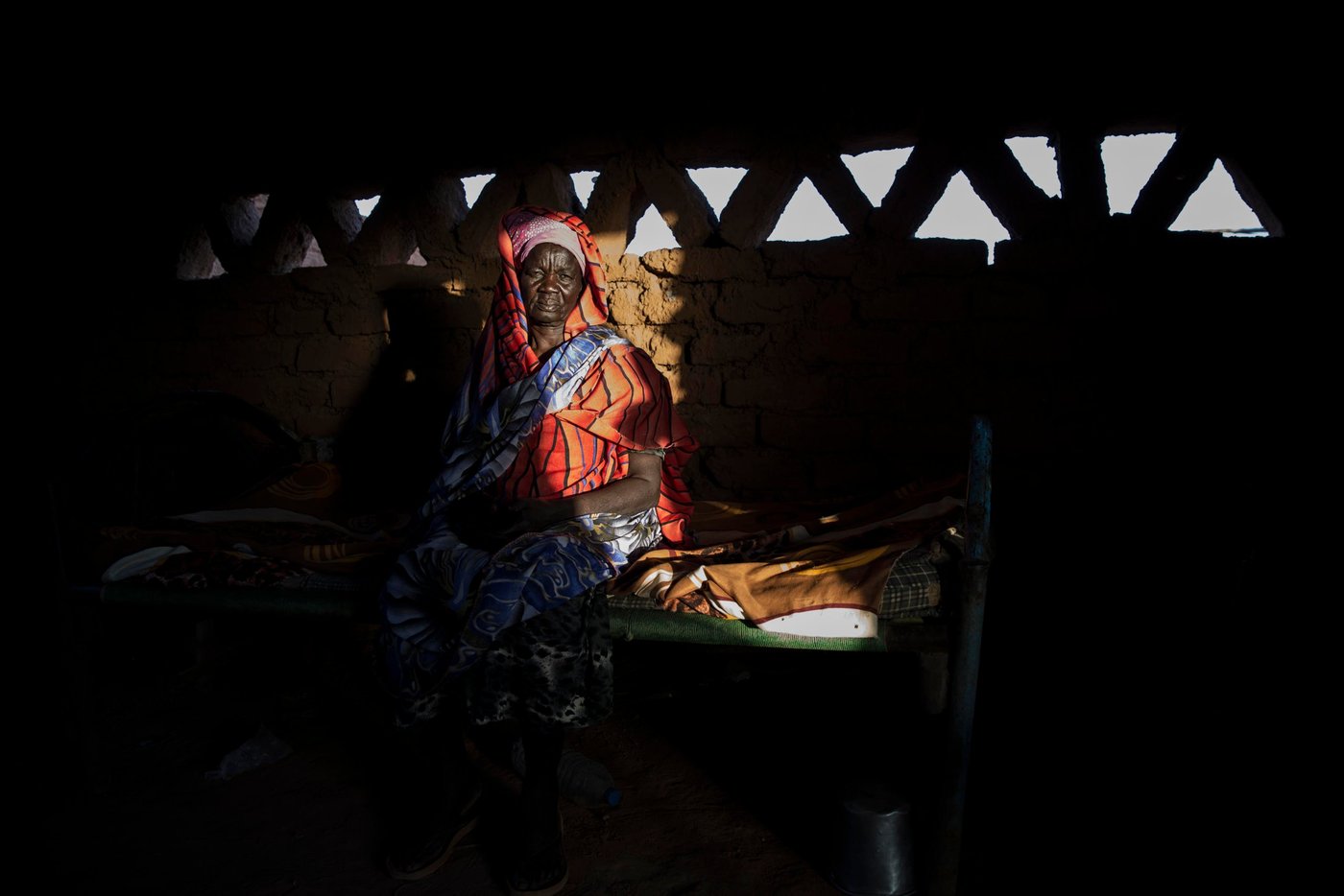 Apuk, 70 year old grandmother in her home. 

Full story:

Anglo Woku never imagined he would be considered a refugee in Sudan in his twilight years. Especially since he left the Southern part of the country for a better life almost 50 years ago.
“I escaped in 1969, shortly after the civil war broke out. I ended up in Khartoum. I was working for the military. I was married, had a family and friends. Sudan gave me a good life,” he said.
The conflict between North and South raged on for 22 years until a peace agreement was brokered in 2005. Then in 2011, the people of the South voted for independence and South Sudan, the world’s youngest nation, was born.
This new dawn however caused all sorts of legal uncertainties for the South Sudanese living in Sudan, particularly in the years following independence.
“I lost my Sudanese identity,” Anglo, 78, explained: “I went from being a public servant to a refugee.”
In 2011 following the independence of South Sudan, Sudan passed laws that had a detrimental impact on the identity of people with Southern heritage.
They automatically lost their Sudanese nationality and were now considered South Sudanese. Even their children, despite being born and raised in Sudan, were given a new nationality. Many people had no intention of returning to South Sudan, a country, largely unknown to them and this created a legal dilemma on questions around their legal status. 
Under the Four Freedoms agreement signed in 2012 between the government of South Sudan and Sudan, South Sudanese were to be granted freedom of movement, residence, economic activity and the right to acquire and dispose property. They were also awarded prima facie refugee status, however the legal status of those who lost their Sudanese identity following the cessation, but with no intention of returning, remains unclear.
Some however made the decision to leave for South Sudan both spontaneously or with the assistance of the UN through facilitated returns.
As part of the organised returns, those willing to repatriate were assembled at departure points. However, in 2013, conflict erupted in South Sudan and the operation was stalled leaving thousands of South Sudanese in limbo and stuck in departure points, to this day.
These departure points, now known as Open Areas, are home to over 31,000 South Sudanese living in nine Open Areas across Khartoum. Anglo is among those languishing in these areas with no rights or access to a decent standard of living.
While registration efforts continue, it is estimated that there are around 154,700 refugees living in nine Open Areas including Um Badda, Jabal Aulya and Sharq El Nile across Khartoum state. They make up approximately 55 per cent of the overall South Sudanese refugee population and are among the most vulnerable members of Sudanese society.
Life is tough in the Open Areas and thousands have limited access to food, water, healthcare or livelihoods. 
“I found myself jobless and homeless with no rights, no identification and I have been here ever since,” Anglo revealed further.
Fondly known as ´the Sultan´, the name given to well-respected leaders in the community, Anglo went from the upper echelons of Sudanese society to being exiled to a dusty, sparce flat land called Nivasha on the edge of Khartoum’s city limits. 
He and thousands more live an invisible existence here, virtually hidden from the rest of the Sudanese population who struggle on with life in a country buckled by years of oppression, debt, government corruption, international sanctions, recurrent drought-related famines and humanitarian chaos. Out of sight and out of mind seems to the policy for urban refugees in modern day Khartoum.
“I did not want to become a refugee. I worked hard as a citizen but this happened. My children have moved back to South Sudan, but my wife is here. My children have jobs and they are safe. We had planned to move back there but there is no way out now. I have no money and we are struck here.”
Like several others, Anglo is a trapped in an administrative quagmire that no organization or agency has the full funding, capacity or support to resolve.
The Commission for Refugees is the body mandated to manage refugee affairs in-country including registration and refugee status determination. It is funded by UNHCR, which maintains a supervisory role, is currently dealing with a backlog on registration. Access to documentation remains a key challenge for all unregistered refugees. Biometric registration is ongoing however it will take time before the backlog is cleared.
The winter sun is setting as we arrive at Nivasha settlement and paints a golden syrupy hue over the far out and forgotten community.
Terra cotta-coloured cuboid homes line the vicinity like blocks on a Tetris game. Curious heads peep out from glassless windows of makeshift shops, indicating some market infrastructure but nowhere near enough to serve the disadvantaged population.
Bells tinkle from under the throats of overburdened donkeys carrying the only available water to the residents. A teenage boy rides on top and raises his thumbs to smile as the camera flashes and lights up the expansive area that will soon be in plunged into darkness.
There is limited electric, running water, and food scarcity plays constantly on the minds of mothers desperate to feed their growing children.
“There is no food,” said 70-year-old grandmother Apuk.
“We are constantly hungry. I have never known hunger until I came to these settlements,” she said.
A handful of local agencies including WFP offer humanitarian assistance to the 11,000 people of the settlement but there are virtually no income-generating activities available to provide a sustainable away from a reliance on aid.
As a result, many residents venture into the nearest neighbourhoods or markets for daily work opportunities. Men find casual labour while the women find cleaning or housekeeping jobs.
“My daughter when she gets work, provides around 50 Sudanese pounds per day (less than a dollar). If we get money, we get a meal once a day. But if she finds no work, we have to search for food in the night to ensure the children get something to eat,” Apuk said.
“We often come home with nothing.”
Like many vulnerable communities around the world, the Covid-19 pandemic has had a crippling economic effect on people fiercely reliant on daily labour wages.
Restrictions and lockdowns forced the city to close and dried up the only work opportunities available to men and women living hand to mouth. The cash-dependent people of Nivasha are no different to the cash-dependents of Naples, Nairobi or New York. Pandemic poverty affects all.
With no adequate health or sanitation facilities around, Nivasha is a welcome host for coronavirus among other diseases. And if anyone is sick, there is no ambulance to take them to a hospital. The nearest hospital is miles away and the only way to travel is an expensive and unaffordable taxi or motorbike ride.
With the recent inflation rate, certain food commodities such as red meat, dairy products and fish are also expensive. Everything is expensive in economically-fragile Sudan.
As Anglo points out, people need more than subsidies to be able to afford to eat, they need opportunity.
“This land is good. It can be productive for food with the use of small backyard land, but the community does not have the support to start food production activities,” he explained.
“If they had their own vegetables, they could eat them and sell them. There are many women here that are farmers. They know what to do. They would like to start farms or shops.”
Apuk reveals that she grew up on a farm in South Sudan and remembers her young life well.
“We had a good life. We had food, plenty to eat. We were fishermen. I miss the taste of fish, I used to eat it every day,” she smiled.
“I feel safe in Sudan but I just want my children to eat. I want them to have some life. I am old but they are not. I have lived and worked in Sudan, but I would like my community to live better,” she said.
Anglo admits life is not what he expected it to turn out but finds comfort in the many friends he has found in the community. As he talks, several men of various ages gather around him in a brotherly circle. “He is a good man,” says George Allam Lolika-Khalil, the Sultan of another camp, “he cares for the community. He tries to make things right for us especially the children.”
Anglo believes that with the new democratic government, Sudan has the potential to grow but he would like to see the refugee community better served and no longer forgotten.
“If they don´t provide livelihood opportunities or training. We will just waste away. We are now known as refugees but many of us have lived here all our life and we just want to continue living without struggling. We just want to feel settled in the country we have always called home,” he said.

Photo: Ingebjørg Kårstad/NRC