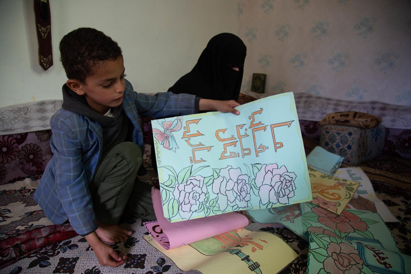 Mohammed showing his mother's art work.
"I am proud of my mom, she is a great teacher who spreads knowledge to the students. I want to become like her - a teacher," Mohammed says.
Mohammed (10) is Rahma's son. He studies in the classroom, but dosen't always have a place to sit.
With support from ECHO, NRC has built new classrooms and wash facilities in the Yemen Al-Mustaqbel school in Sana’a.The new classrooms will accommodate an additional 500 students next school year.
NRC’s education programmes in Sana’a seeks to ensure that children affected by war have continued access to school. This includes displaced and host community children. NRC covers teacher incentives, repair buildings, train teachers and provide educational resources like desks and books.
Photo: Mohammed Awadh/NRC