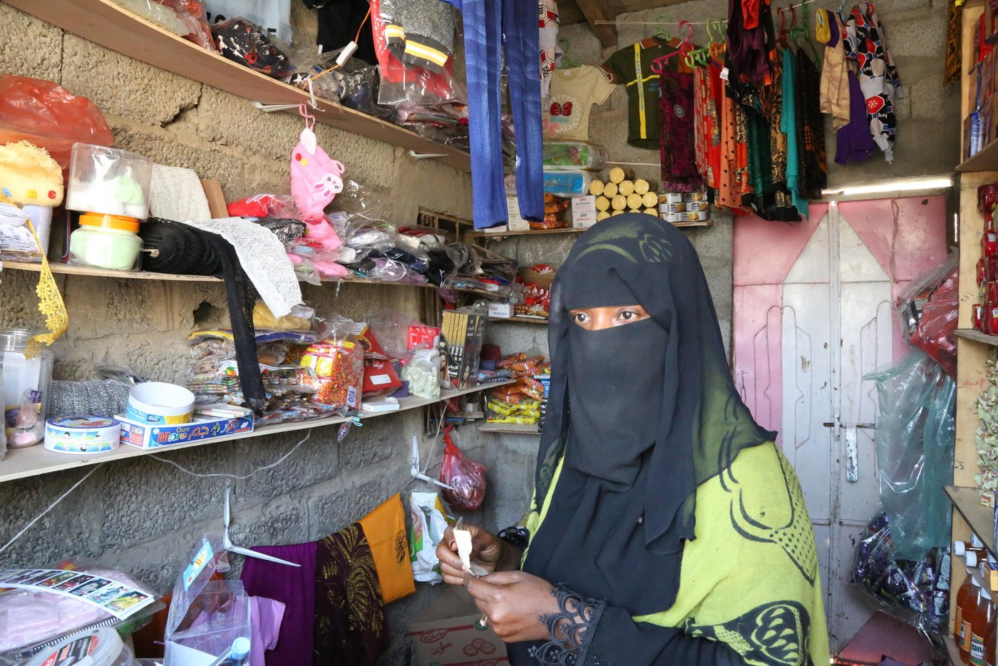 “My husband was the breadwinner for the family,” Asma Abdullah Saleh explains. A mother of three, her husband had been hiring himself out as a labourer. But then his work dried up, leaving the family struggling.

Unable to watch her children going hungry, Asma decided to act.
First, she started a small lunch business from her home. “I prepared sandwiches, which I sent my children to sell to the students in the nearest school.”

Asma had some experience in hairdressing, so she tried that too. Unfortunately, weddings—the main source of hairdressing demand—happened rarely in her small village. “I tried different jobs, including sewing dresses,” Asma explains.
 
But even with the whole family helping out, it wasn’t enough. “We used to buy food on a daily basis. We couldn’t afford to buy for the week.” She was also worried that her children’s education was suffering because of the time spent selling sandwiches.

Then Asma was selected to receive the small business training from NRC. “NRC asked me to dedicate a room in my house to establishing my own small project,” Asma recalls. “I used to have some jewellery, so I sold it and built a small room, and started my little shop.”

At first, Asma was only able to sell the most basic items to her customers, as the shop was very small. But the training also came with a grant.
 
With this, “I could buy more goods and my shop became larger than before. Nowadays, when a customer requires an item, I can buy it from the market and sell it to them.”

Though small, Asma’s shop quickly became the family’s main source of income. “I feel happy that I can provide my family with enough food. And I feel even happier that my children [can] attend school now to study only, and don’t have to sell sandwiches anymore.”

Covid-19 has been devastating for many markets and job sectors, but the relatively isolated location of Asma’s village has worked in her favour, with few cases reaching their area. In recent months business has remained good, and she has been able to add more stock lines than before.

“It is true that the shop is better now,” she acknowledges, “but I’m still working hard to make it even larger!”

This project was funded by the French Ministry for Foreign Affairs, as part of our efforts to provide more sustainable and long-term solutions to the humanitarian crisis in Yemen. NRC also provides frontline emergency support to families in immediate need of live-saving assistance.

Photo: Nasser Abdulkareem/NRC
