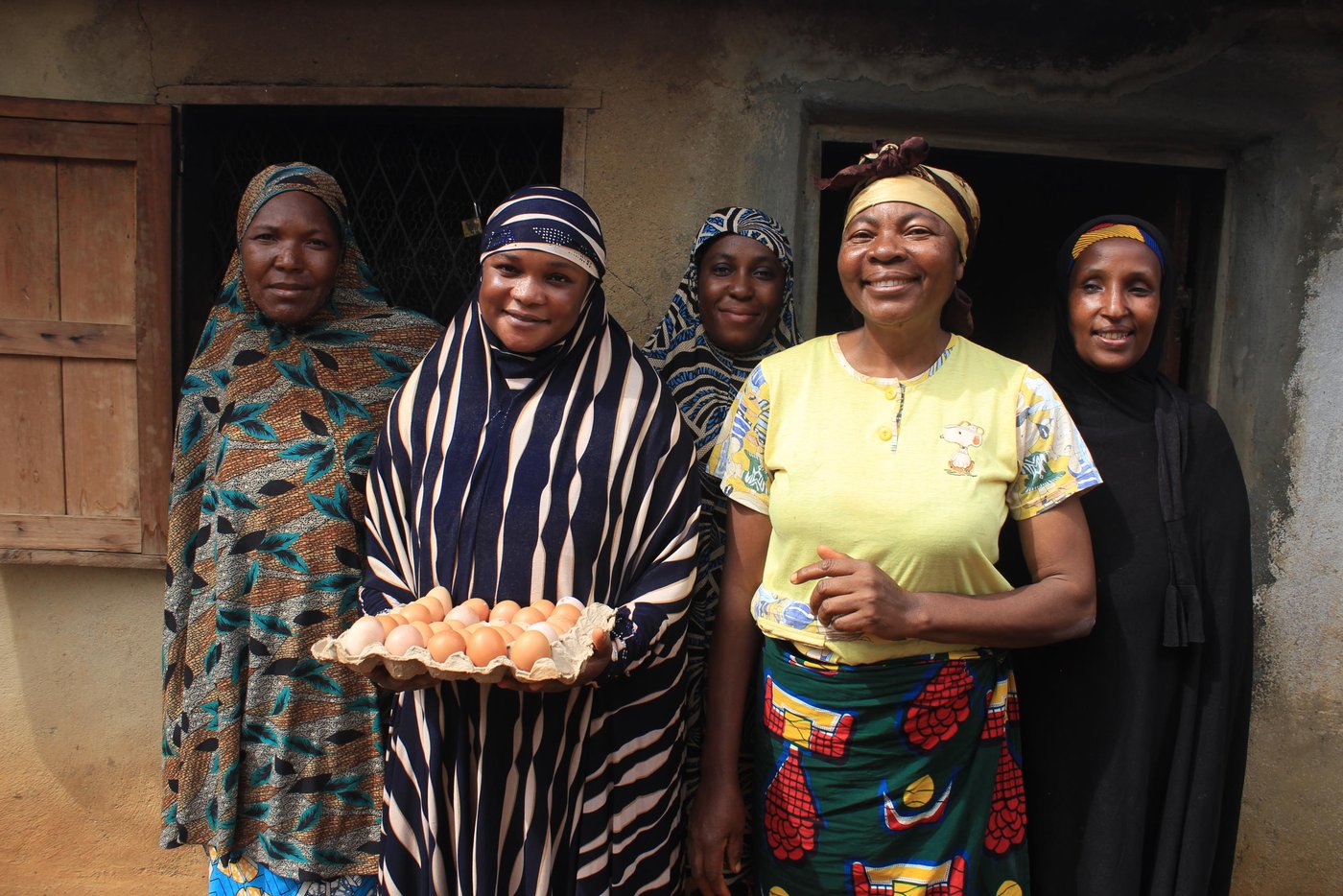 A group of women on their way out of a building. They are all smiling. One of them is holding a tray of eggs.