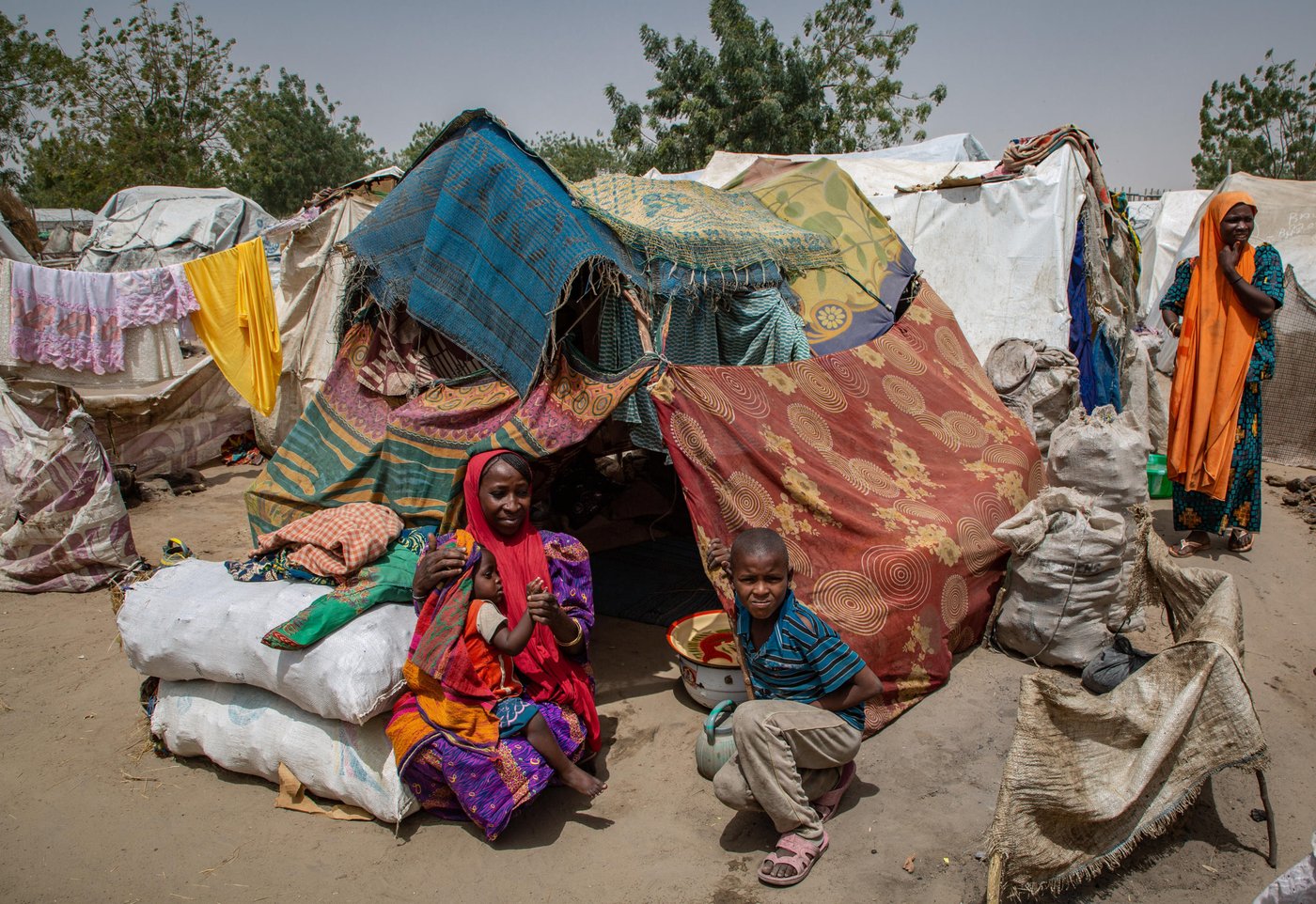 Bilkisu and her children sitting in front of their makeshift tent - Ngala reception center.
''In the last 6 years, I’ve been forced to move three times. The first two times I was fleeing violent attacks, and then the third time because of floods,” says Bilkisu, 33, a mother of three living in Ngala reception center.
"I don't even recall how many months we have been here, my husband and my son built our hut with the support of some other people and we have been living there since then. We have nothing but this hut and some coal to make fire."
Bilkisu and her family are part of the 7,000 people crammed in Ngala reception center. The overcrowding of camps in NE Nigeria entails alarming living conditions, with a general lack of basic hygiene and water facilities, with families sometimes forced to sleep in the open or cram themselves into makeshift shelters or tents. In these conditions, implementing the basic measures of hygiene is more than challenging.
''Most of the people here have been defecating in the open, usually running to the nearby bush. Some of the tents are just next to ponds full of crap and feces, I tell my children to stay away so they don't get sick." she says
Taken: 10 March 2020
Photo: Tom Peyre-Costa/NRC