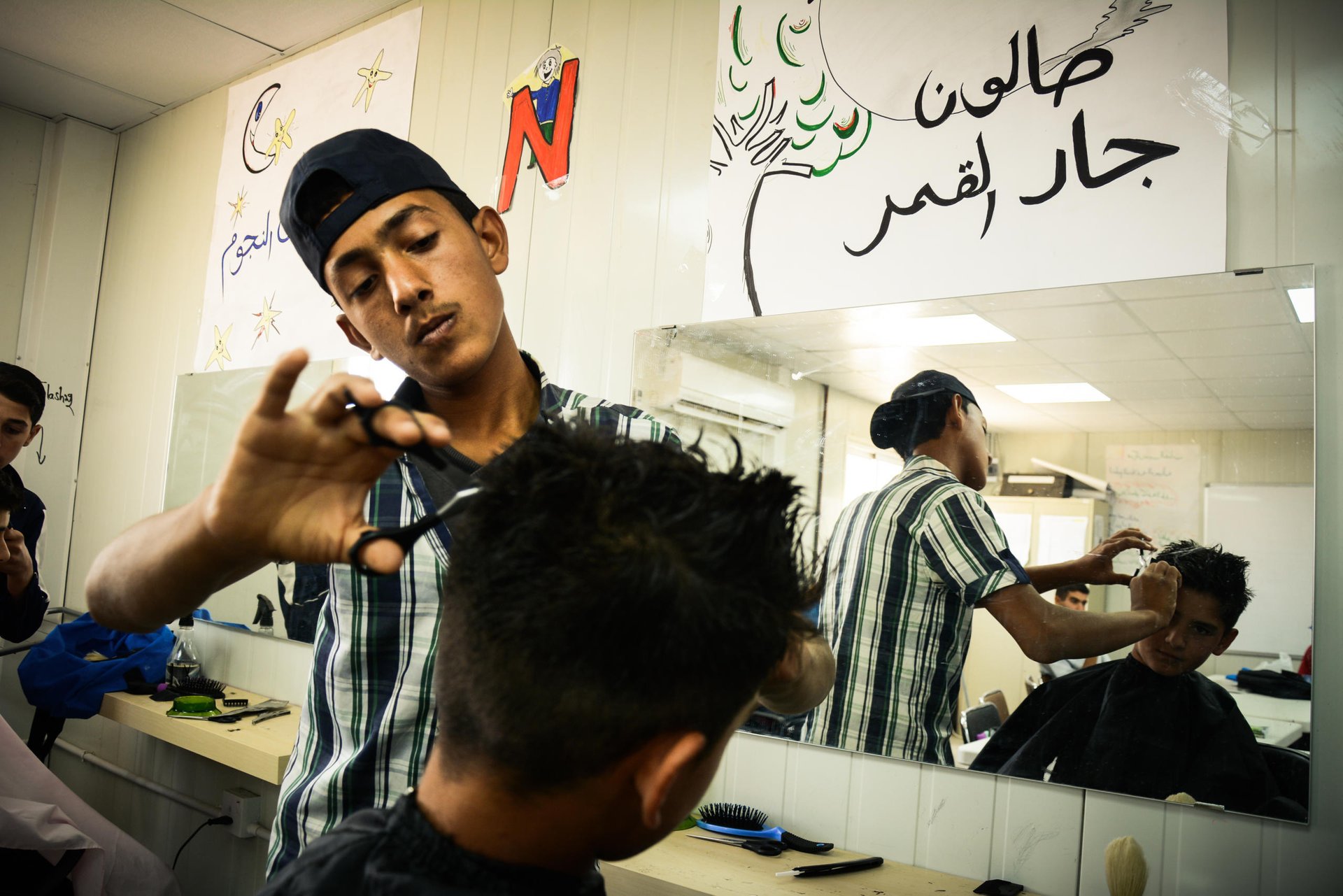 Ameer*, a 14-year-old boy having his hair cut by a Syrian refugee youth at NRC's youth training centre in Azraq refugee camp in Jordan.
Ameer told us that he wants to be enrolled in this course because he used to work in his father's barber shop back in Syria, and would like to learn more here. Since he attends school in the camp, and does not fit the target age group for the centre, he cannot enroll. "Well, hopefully I can practice this skill when I'm back in Syria instead of here", says Ameer.
The youth training centre allocates one day each month for camp residents to come and have a free haircut at the site.
*NRC changed all the names to protect the identity of those featured in this piece
July 1, 2015
Hussein Amri / NRC Jordan