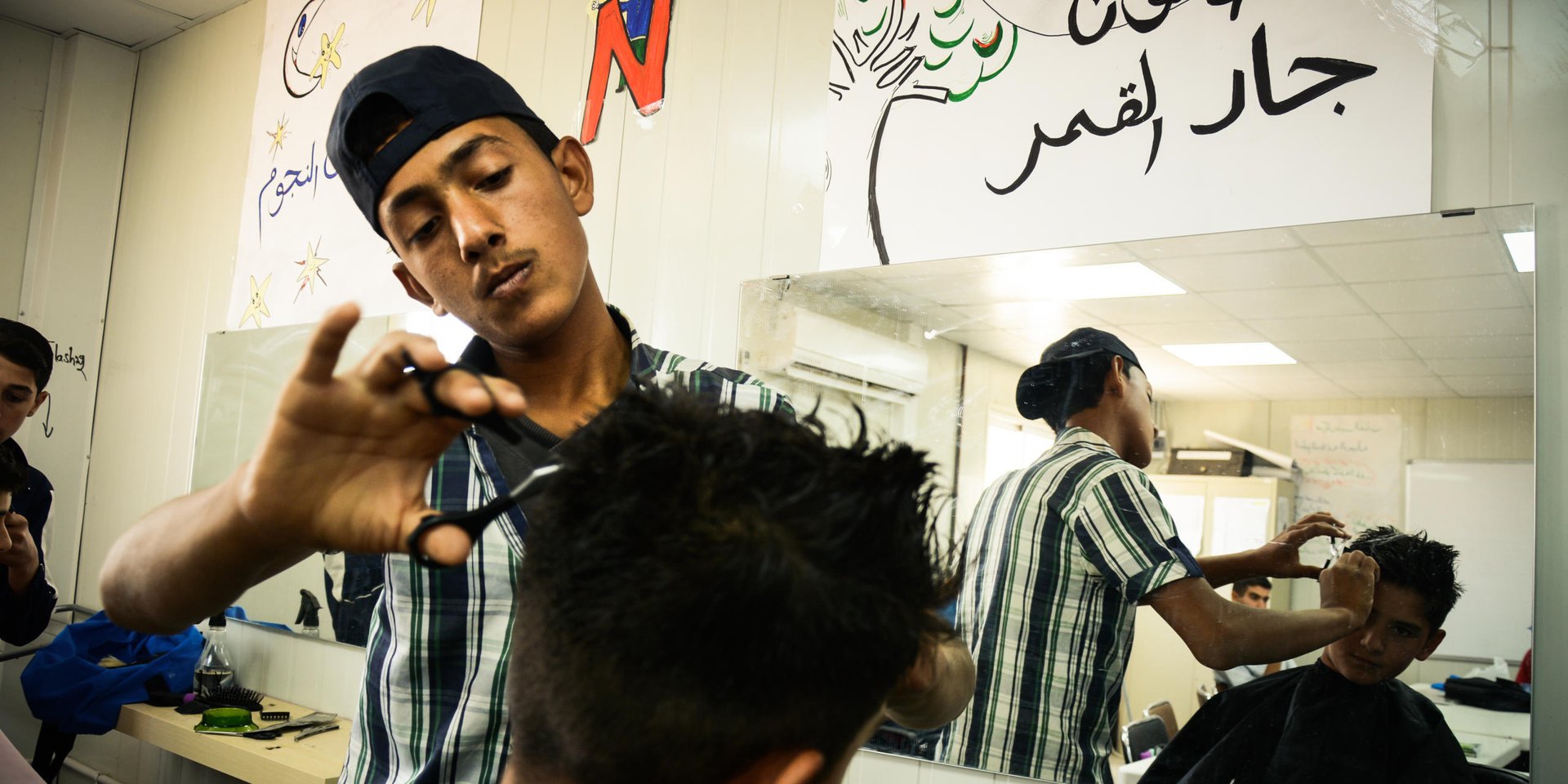 Ameer*, a 14-year-old boy having his hair cut by a Syrian refugee youth at NRC's youth training centre in Azraq refugee camp in Jordan.
Ameer told us that he wants to be enrolled in this course because he used to work in his father's barber shop back in Syria, and would like to learn more here. Since he attends school in the camp, and does not fit the target age group for the centre, he cannot enroll. "Well, hopefully I can practice this skill when I'm back in Syria instead of here", says Ameer.
The youth training centre allocates one day each month for camp residents to come and have a free haircut at the site.
*NRC changed all the names to protect the identity of those featured in this piece
July 1, 2015
Hussein Amri / NRC Jordan