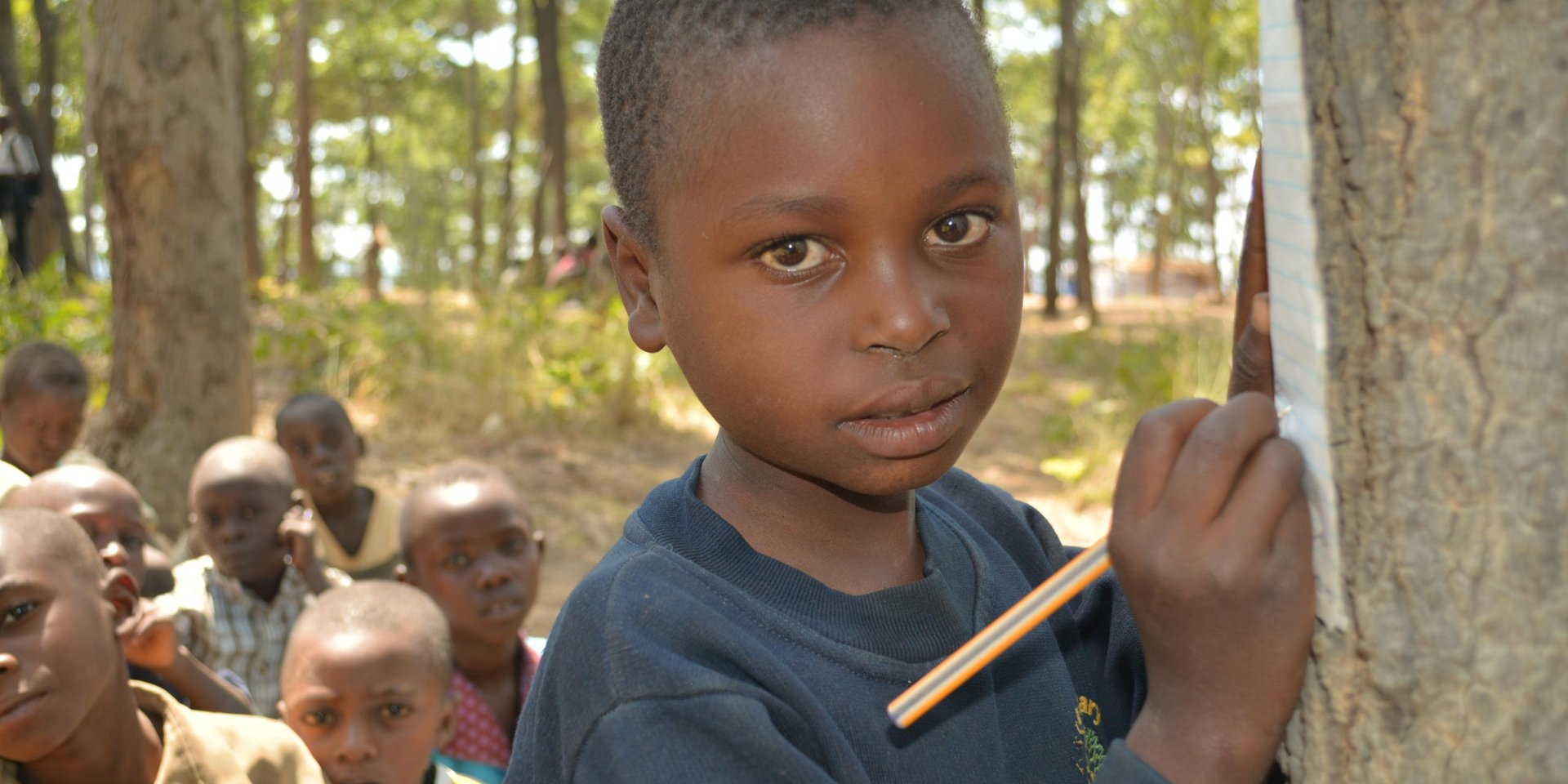 Kevine's teacher is called Benjamin. She likes to read and write in Swahili. She wants to become a teacher when she grows up.
“I would like to share knowledge with others and help them grow,” she says. But she lacks pens, exercise books. She has to borrow papers and pencils from her classmates if they have extras. Sometimes she borrows from the teacher if he has additional materials.
She is sitting in the classroom with her classmates. They study under the trees. She feels that it is very hard to concentrate because of the passing cars. The dust also interferes with her concentration. The classes are so close to each other that she can hear what is being discussed in the other classes. This makes it hard to focus on her studies.
She misses her school life back in Burundi. She used to study in real school building made of cement and had enough learning materials.
Her quotes:
“What I like at school is Mathematics and writing.”
“What I like most is Mathematics and Writing.”
“What I like most is to go to school to study Mathematics, to study writing, I want to be a teacher.”
“I feel sad because I do not have materials; exercise books and pen and clothes and shoes and school bag.”
“I feel very sad because I do not have anything.”
“Back home I used to study, I continued studying but because of conflict I stopped going to school.”
“In Burundi, we were studying in school buildings. They had cement floor and chairs. But here, we study under trees and we sit on stones.”
“We find it hard to concentrate when a car passes, students stop studying and focus on the car.”
“I am missing exercise books, clothes, pens and shoes. I am missing them.”
Photo: NRC/Ingrid Prestetun