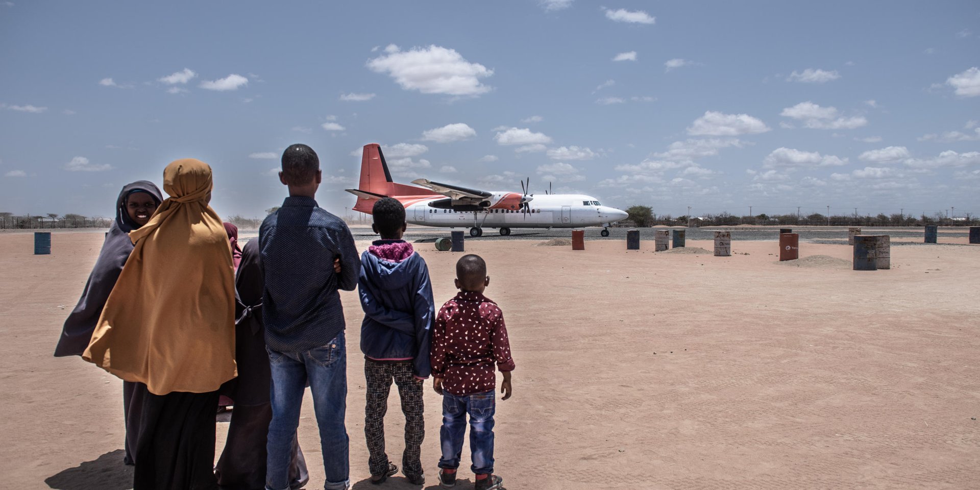 A Somali family looks on as a plane arrives in Dadaab refugee camp to take them back to Mogadishu, Somalia. 

They are one of 40 families returning today as part of the voluntary return programme. 

About 23,000 refugees who have left Dadaab camp this year to return back to Somalia. They are part of a return programme set up by the UN’s refugee agency and the Government of Kenya. NRC is working to ensure that people returning to Somalia are given information about the areas they are going to, and that process is well coordinated and returnees are protected. 
 
Date: September 2016

Photo credit: NRC/ Fredrik Lerneryd
