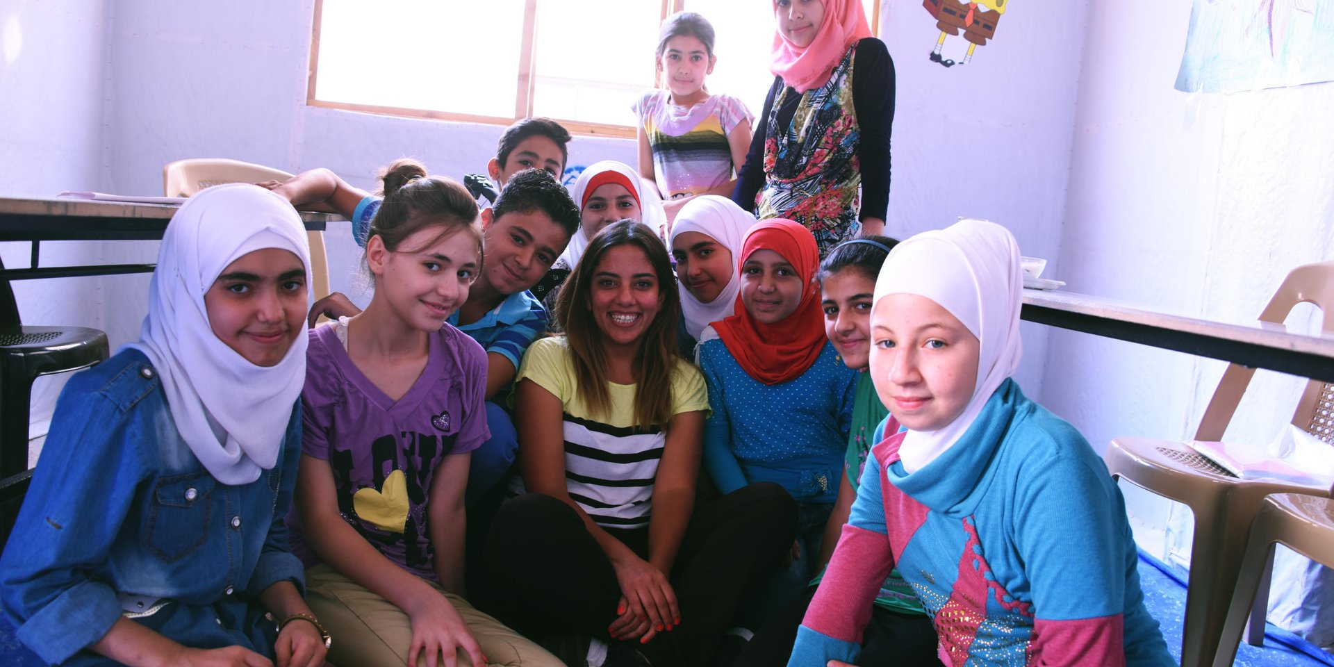 NRC Education Officer Walaa Aalam surrounded by children attending the Centre for children in Sahnaia on the outskirts of Damascus.
Walaa said: “The value this Centre is providing to these children is so important. They have a safe environment to learn and to play in, which they are really lacking. This initiative provides children, who have left their homes and everything they knew, with an open door to education, school and a future. There is such a positive energy here. I always come out smiling.”
Supported by NRC, the centre is run by a community-based association which assists around 150 displaced children from across Syria and others from the community catch up on their education. The centre runs catch-up classes for children and hosts recreational and life skills activities through its Summer Programme for children who have been out of school because of the crisis and displacement. Children are prepared to pass government-recognised exams in Arabic, Maths and English so they can eventually return to formal schools. NRC also helps to facilitate a vital link between this community-based initiative and the Ministry of Education.
NRC has been supporting the centre since June 2016, providing student backpacks and supplies, teaching materials, teacher training, and providing administrative support to the association.
Photo: Karl Schembri/NRC
24 August 2016