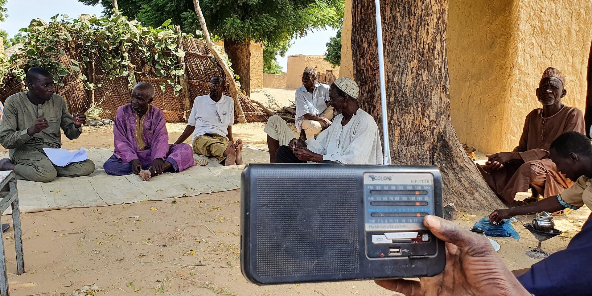 A radio in front of a group of men gathered under a tree in a rural village in Niger.
