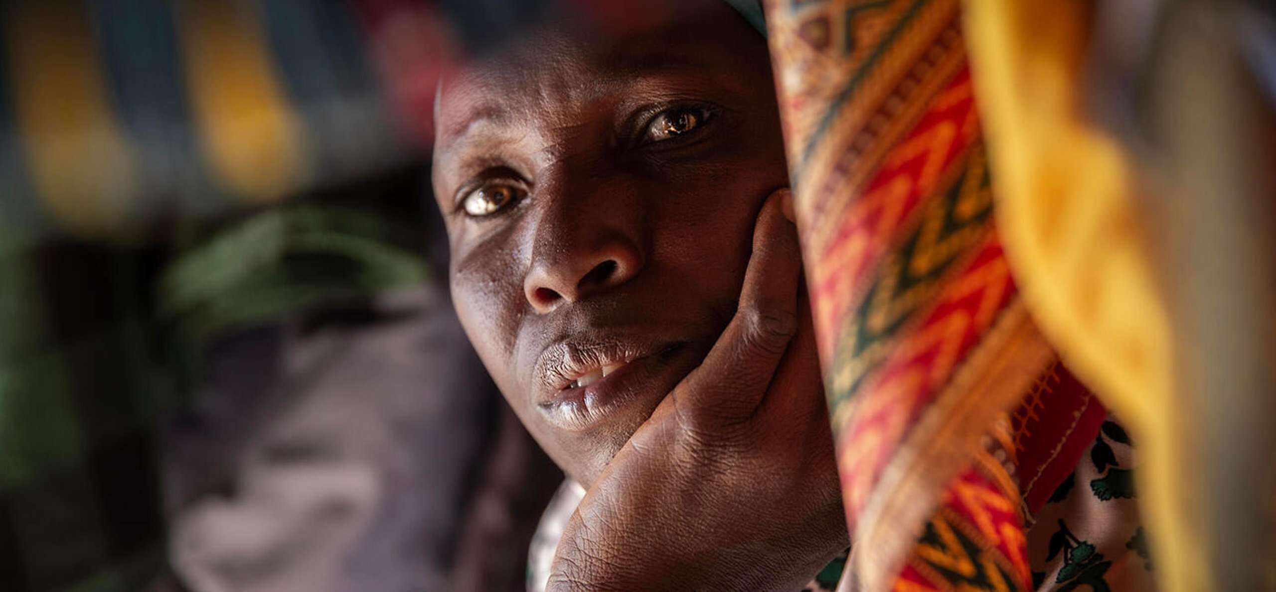 Portrait of a woman resting her head in her hand, surrounded by colourful fabric.