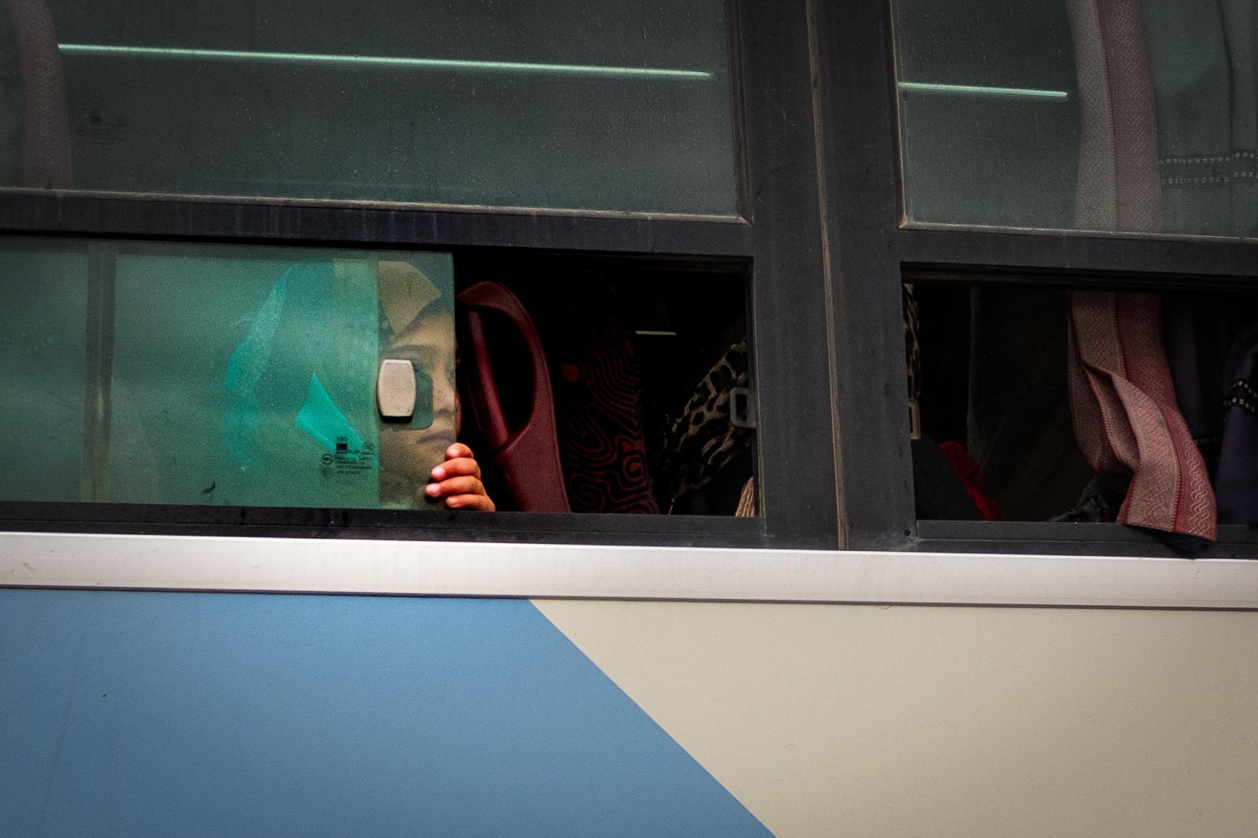 A young girl looks out the window of a bus as it arrives in the Hamam al-Alil camp for people displaced from Mosul. - NRC/Wolfgang Gressman