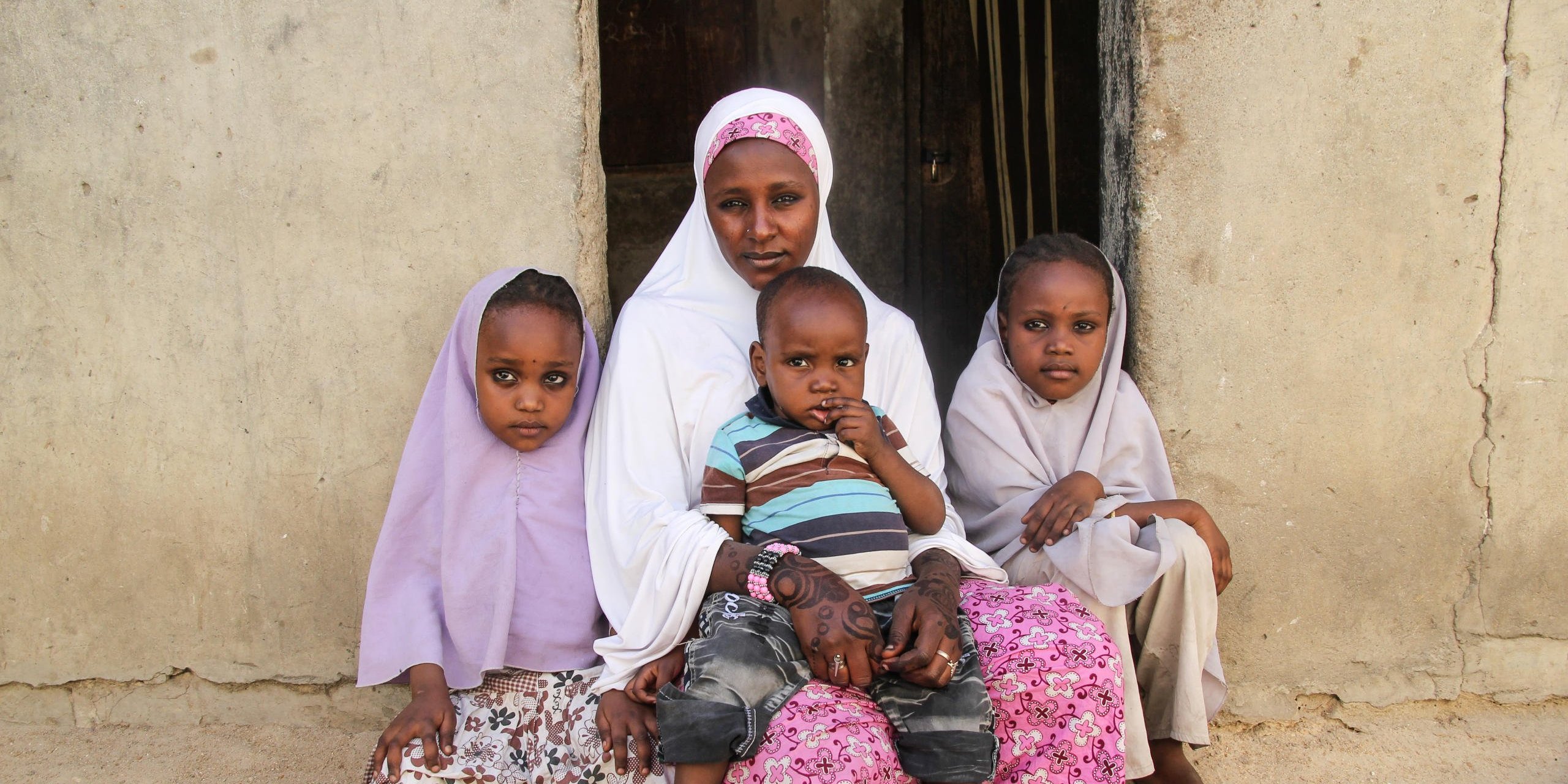 Maryam-27 years old with her daughters Fatima(left), Hafsat(right) and last son Goni-2 years old(on her laps). They were displaced from their town and are now living in Bulabulin. She is a widow who wants to go to school together with her children.
Maryam is a 27 years old mother of 4 from Mafa. She vividly recalls how insurgents invaded their town and started shooting, killing people and burning houses. Her husband was slaughtered in her presence. She had to take away her children and flee for safety. While fleeing, she was afraid something bad might happen to her and her children. They spent 2 days in the bush without food and water but on the third day, they got a vehicle which safely transported them to Maiduguri. She is presently living with relatives who are assisting her and her children because she doesn’t have any source of livelihood at the moment.
She feels safe here and cannot go back home because she has no husband. Whenever she thinks about the death of her husband and the education of her children, she can hardly sleep. Her major needs are food, clothes, education for herself and her children. It is her wish that she and her children will get the opportunity to enrol into school and also get something she can do to enable her take care of her children.
Some of Maryam quotes:
“Our town was invaded and there were shootings and killings and burnings, they started killing men then my husband was slaughtered in my presence”
“I cannot go back to the town because they have killed my husband and there is still no peaceful living in the town”
“Now our needs is that we don’t have enough food, we don’t have enough clothes to wear and I want to enroll them into school”
“My wish is for my children to get educated so they can be useful and also can get a job so that it will be useful to them in the future”
Photo: NRC/Ingrid Prestetun