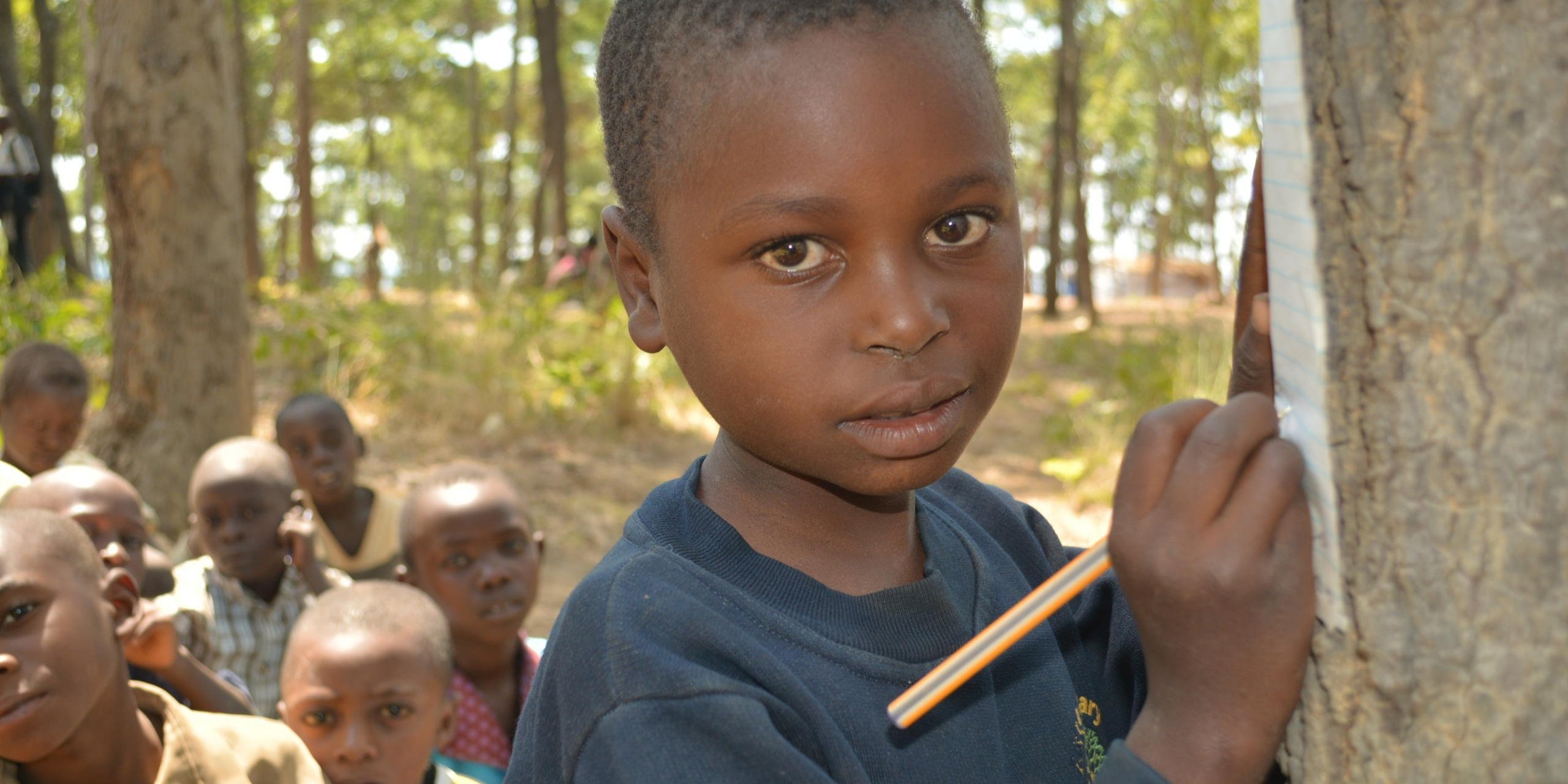 Kevine's teacher is called Benjamin. She likes to read and write in Swahili. She wants to become a teacher when she grows up.
“I would like to share knowledge with others and help them grow,” she says. But she lacks pens, exercise books. She has to borrow papers and pencils from her classmates if they have extras. Sometimes she borrows from the teacher if he has additional materials.
She is sitting in the classroom with her classmates. They study under the trees. She feels that it is very hard to concentrate because of the passing cars. The dust also interferes with her concentration. The classes are so close to each other that she can hear what is being discussed in the other classes. This makes it hard to focus on her studies.
She misses her school life back in Burundi. She used to study in real school building made of cement and had enough learning materials.
Her quotes:
“What I like at school is Mathematics and writing.”
“What I like most is Mathematics and Writing.”
“What I like most is to go to school to study Mathematics, to study writing, I want to be a teacher.”
“I feel sad because I do not have materials; exercise books and pen and clothes and shoes and school bag.”
“I feel very sad because I do not have anything.”
“Back home I used to study, I continued studying but because of conflict I stopped going to school.”
“In Burundi, we were studying in school buildings. They had cement floor and chairs. But here, we study under trees and we sit on stones.”
“We find it hard to concentrate when a car passes, students stop studying and focus on the car.”
“I am missing exercise books, clothes, pens and shoes. I am missing them.”
Photo: NRC/Ingrid Prestetun