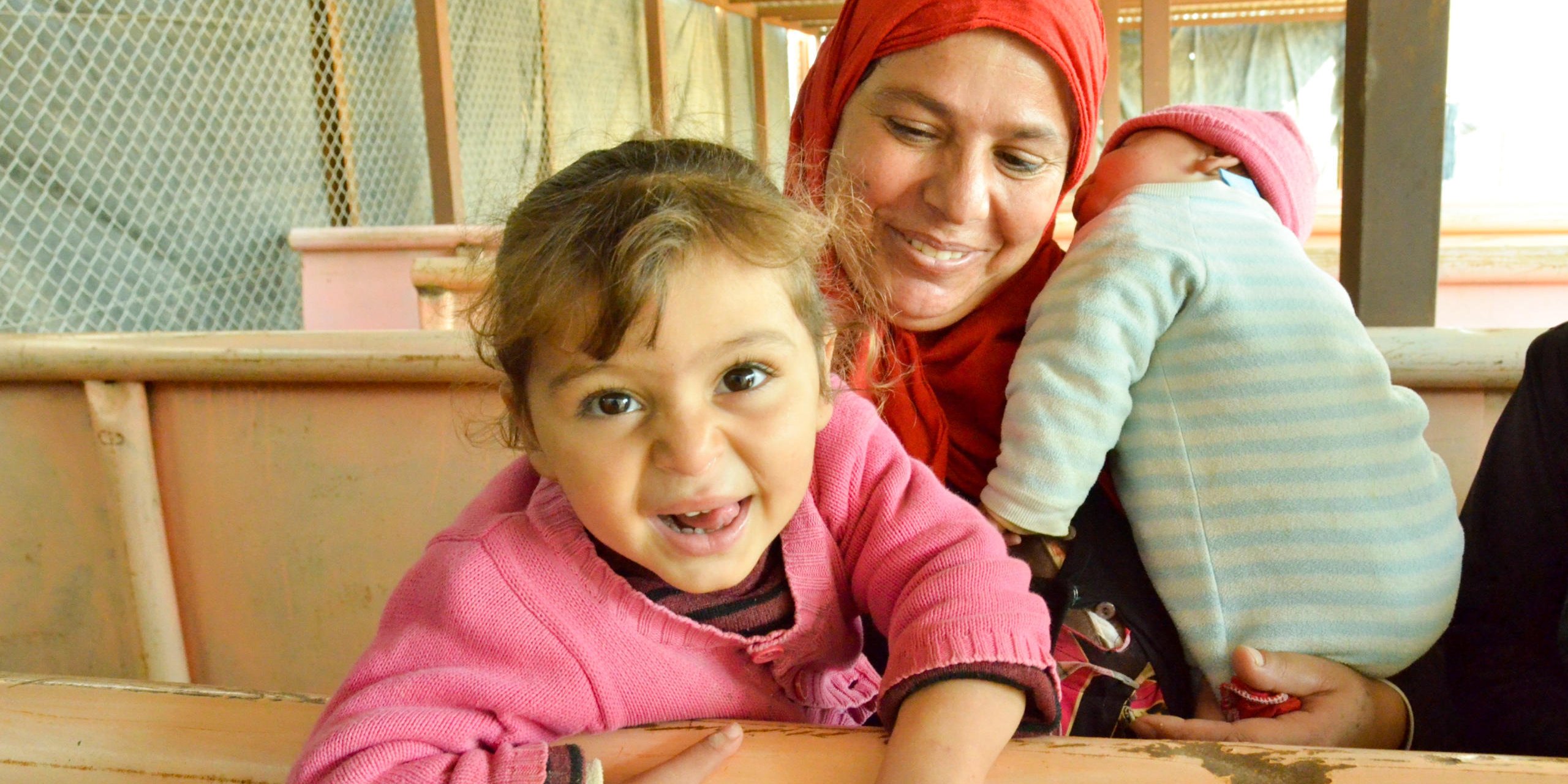 Warda is 2.5 years old and very excited to have her photo taken! She is waiting in line for a voucher together with her mother Aidda and sister Rasha (3 months). Aidda says the family will spend the money on clothes, because they wore out all their clothes on the way to Azraq. They have other vouchers to use for food. Photo taken at a distribution of vouchers to Syrian refugees in Azraq refugee camp on November 17, 2015. Refugee families were given a 10JD voucher that can be spent on what the families need the most, such as clothes for winter. Photo: NRC/Guri Romtveit