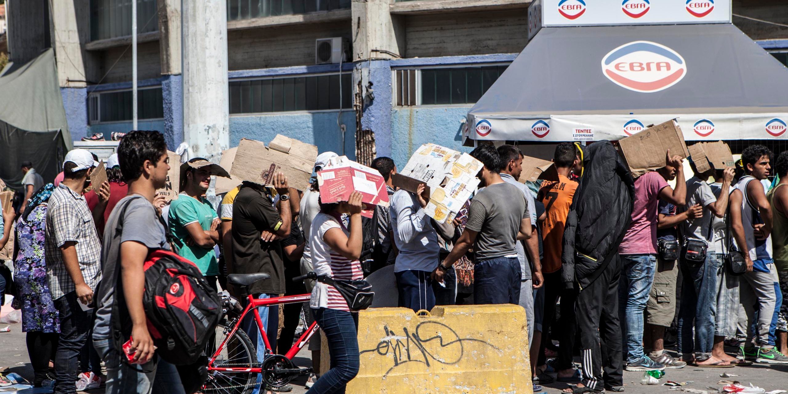 Refugees on Lesvos hiding from the heat while queuing to get tickets for the ferry to Athens. (Photo: Raymond Aaserud/NORCAP)
