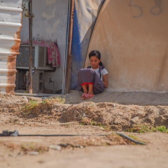 A girl sits and reads outside of her family’s tent at an informal settlement.