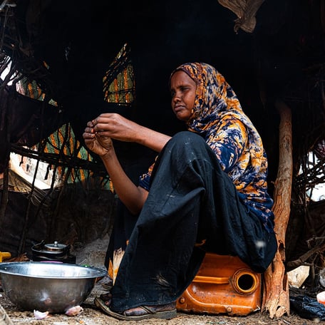 How the Middle east crisis is deepening hunger in Somalia. A woman is sitting on a jerrycan in her shelter, preparing food.
