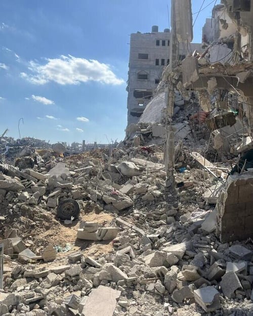Sönderbombade byggnader och stora mängder bråte i ett bostadsområde i Gaza, med blå himmel i bakgrunden.
