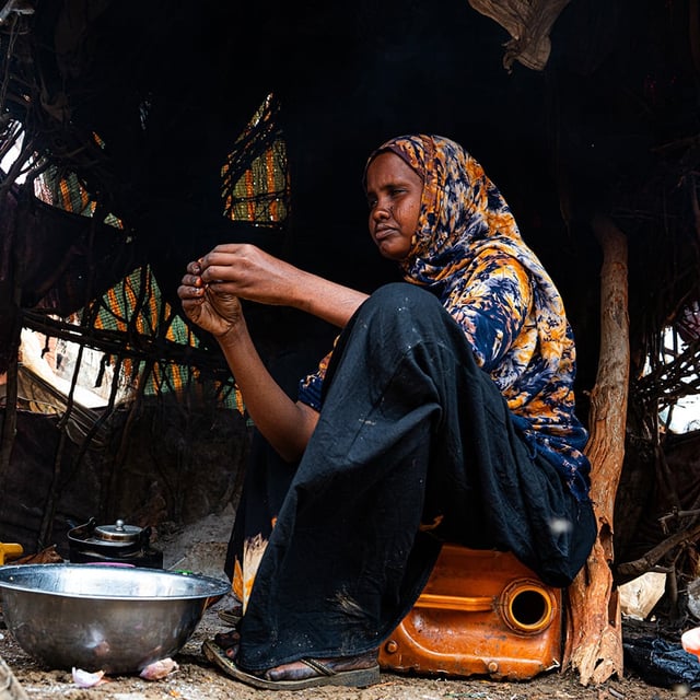 How the Middle east crisis is deepening hunger in Somalia. A woman is sitting on a jerrycan in her shelter, preparing food.