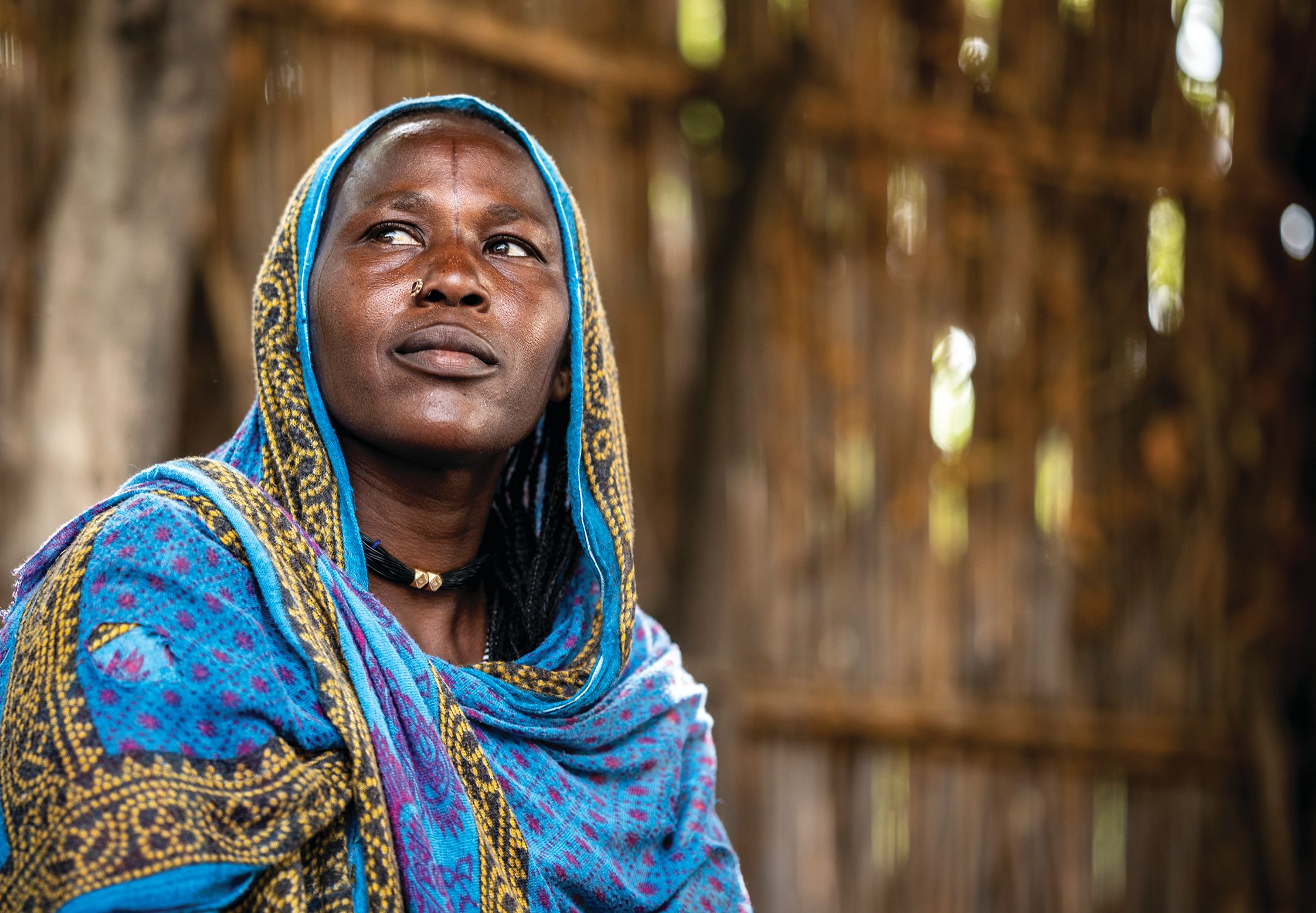 Woman with nose piercing and a blue shawl draped around her head and shoulders.