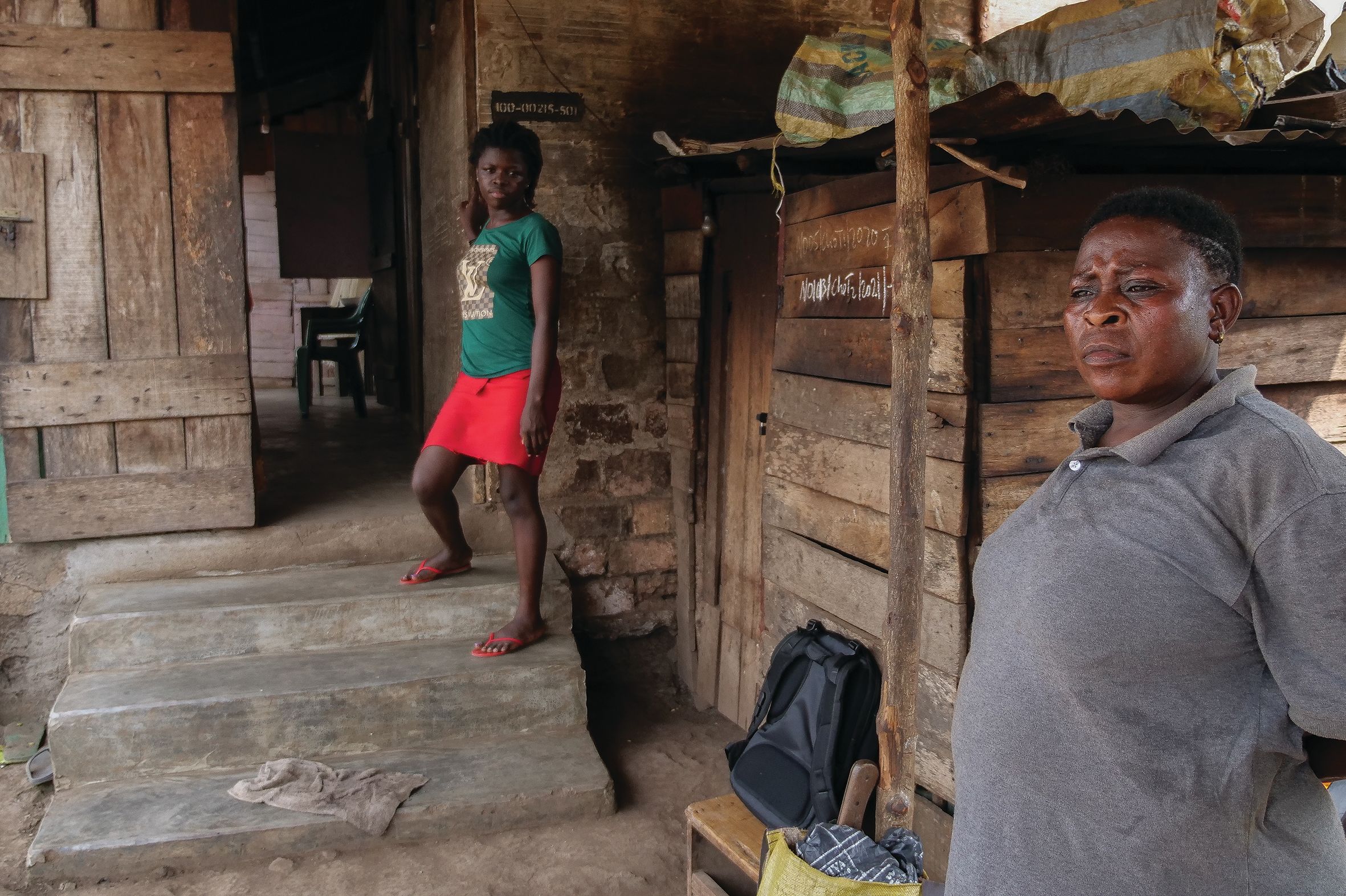 Two women stand outside the small house that they live in.