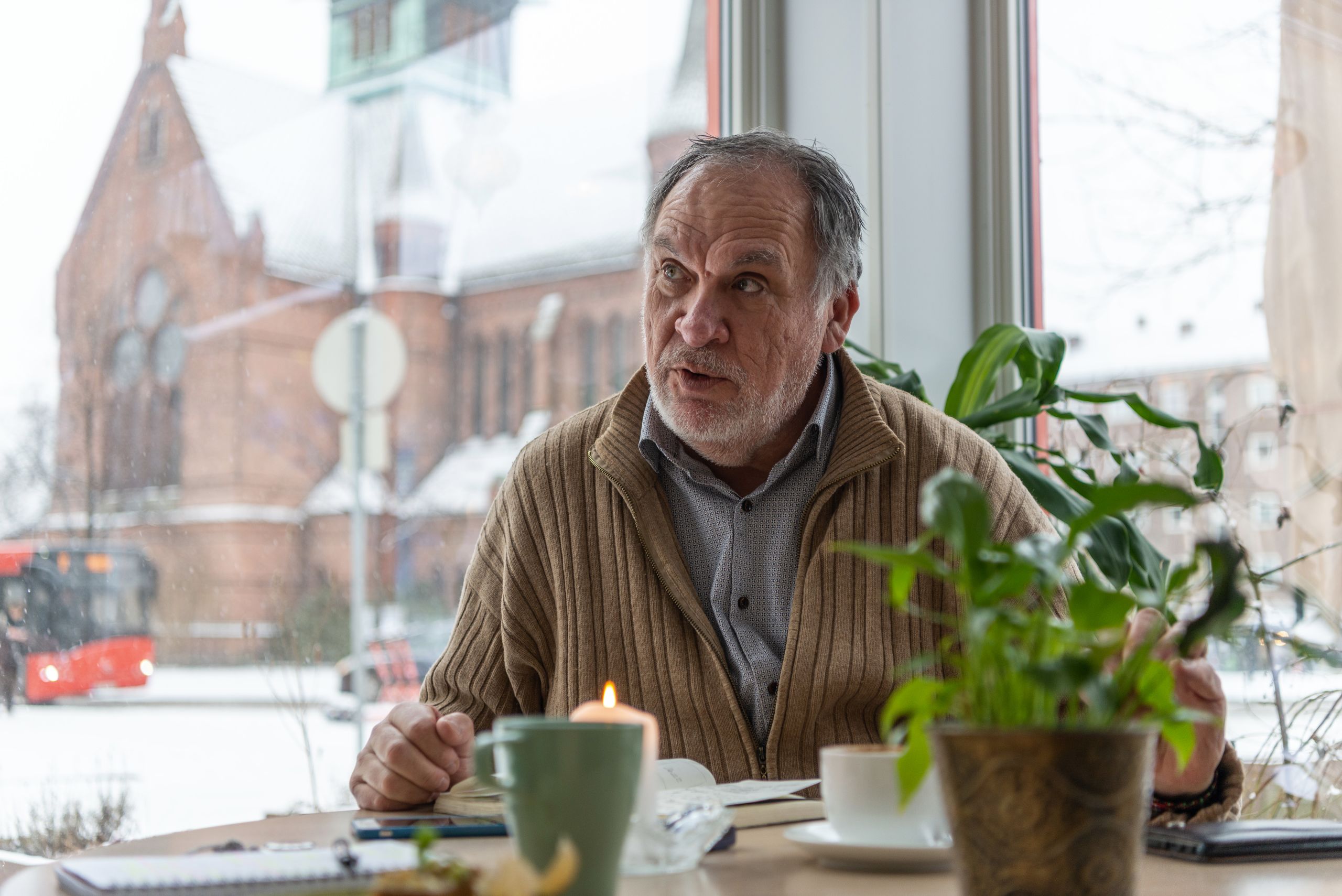 Alfredo telling his story. On the table in front of him is a potted plant, a candle and his coffee mug.