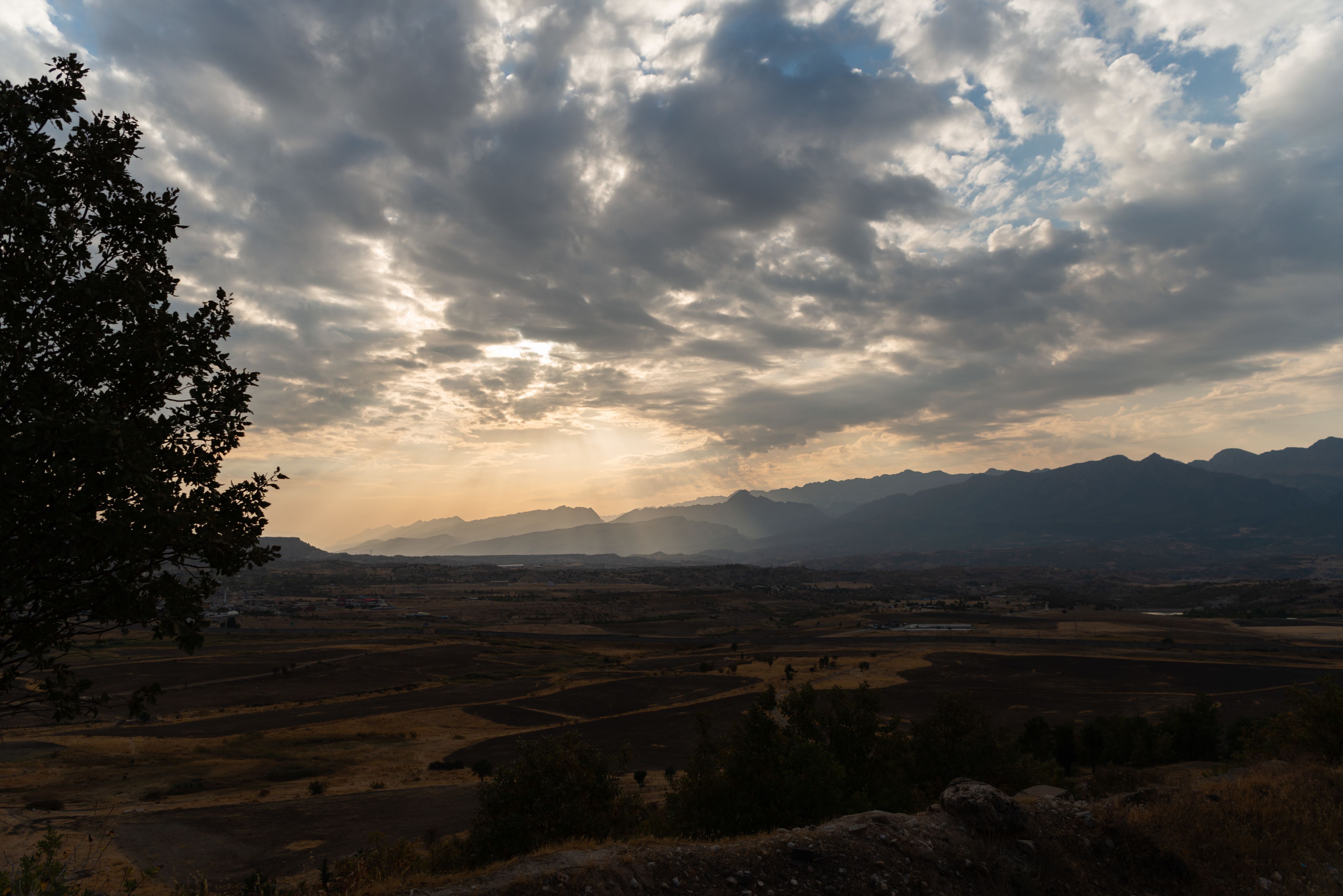 A mountainous valley with soft sun in the background.